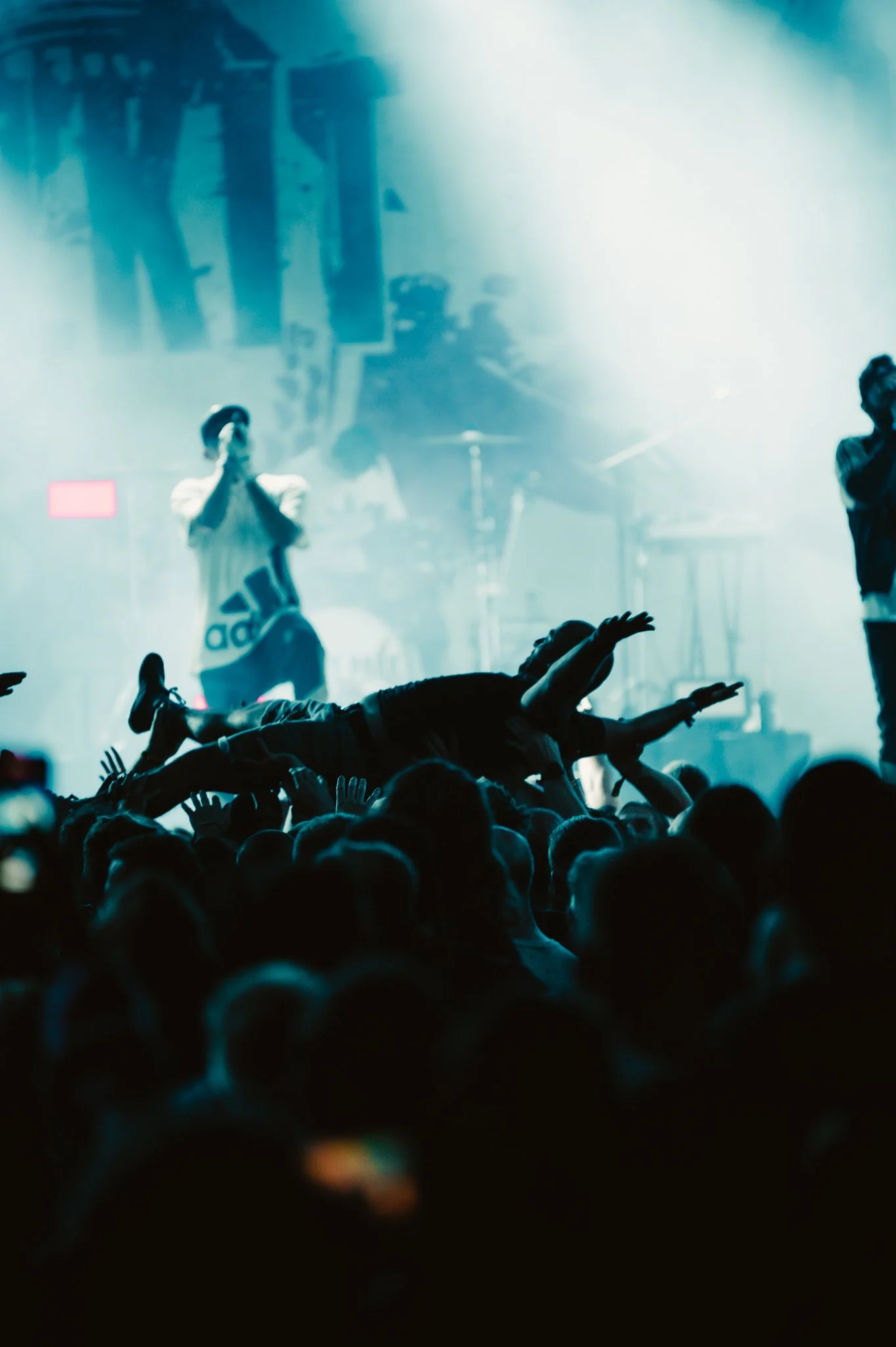 concert with crowd surfing, singer and band performing on stage with blue lighting