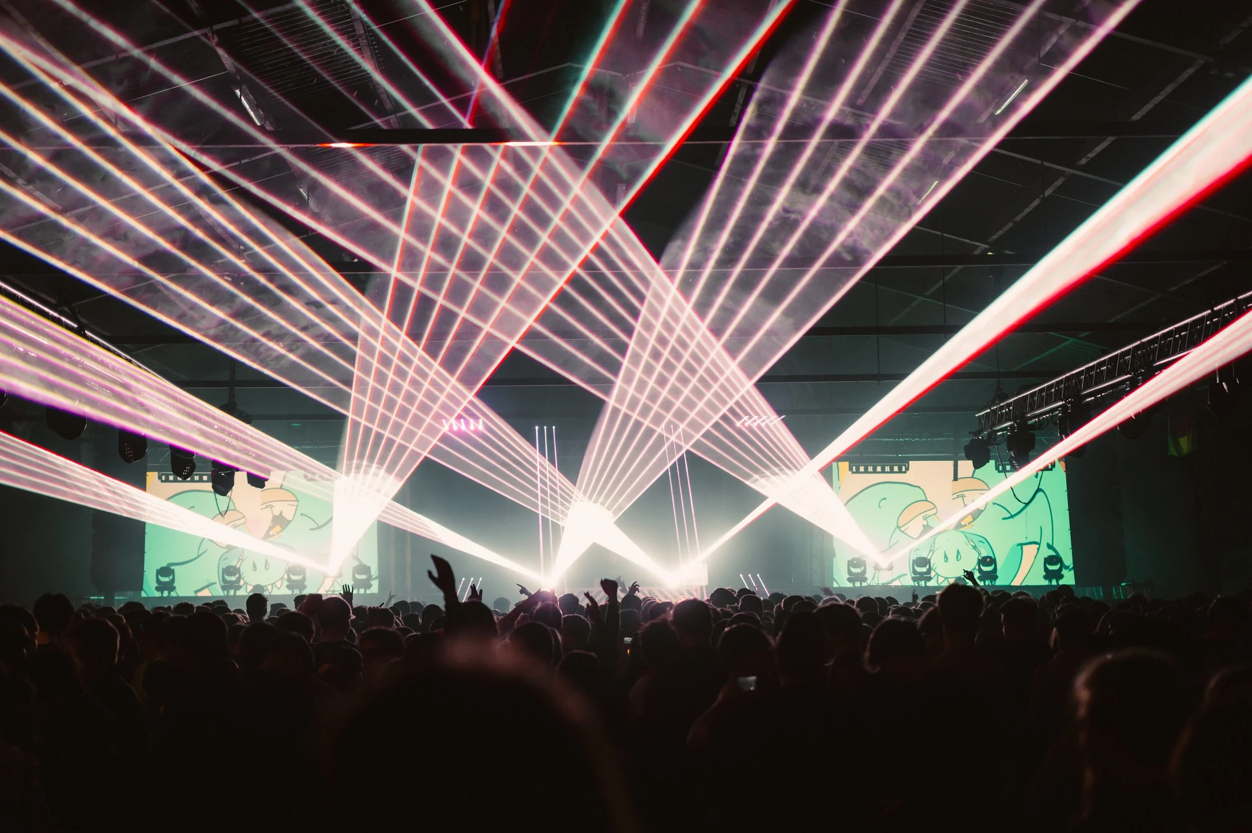 Concert crowd with laser light show and animated visuals on screen.