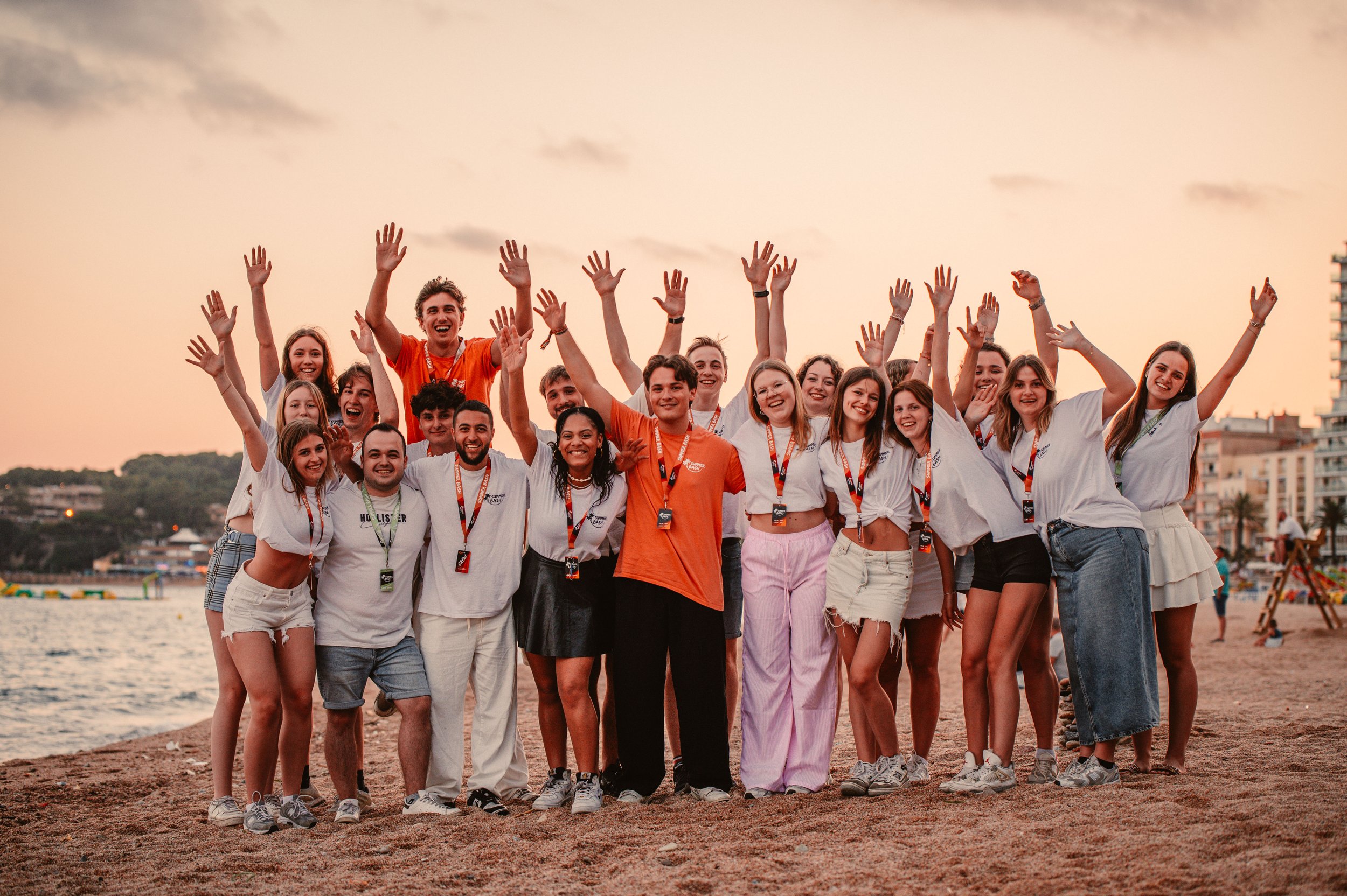 Group of people posing on a sandy beach at sunset, some wearing lanyards.