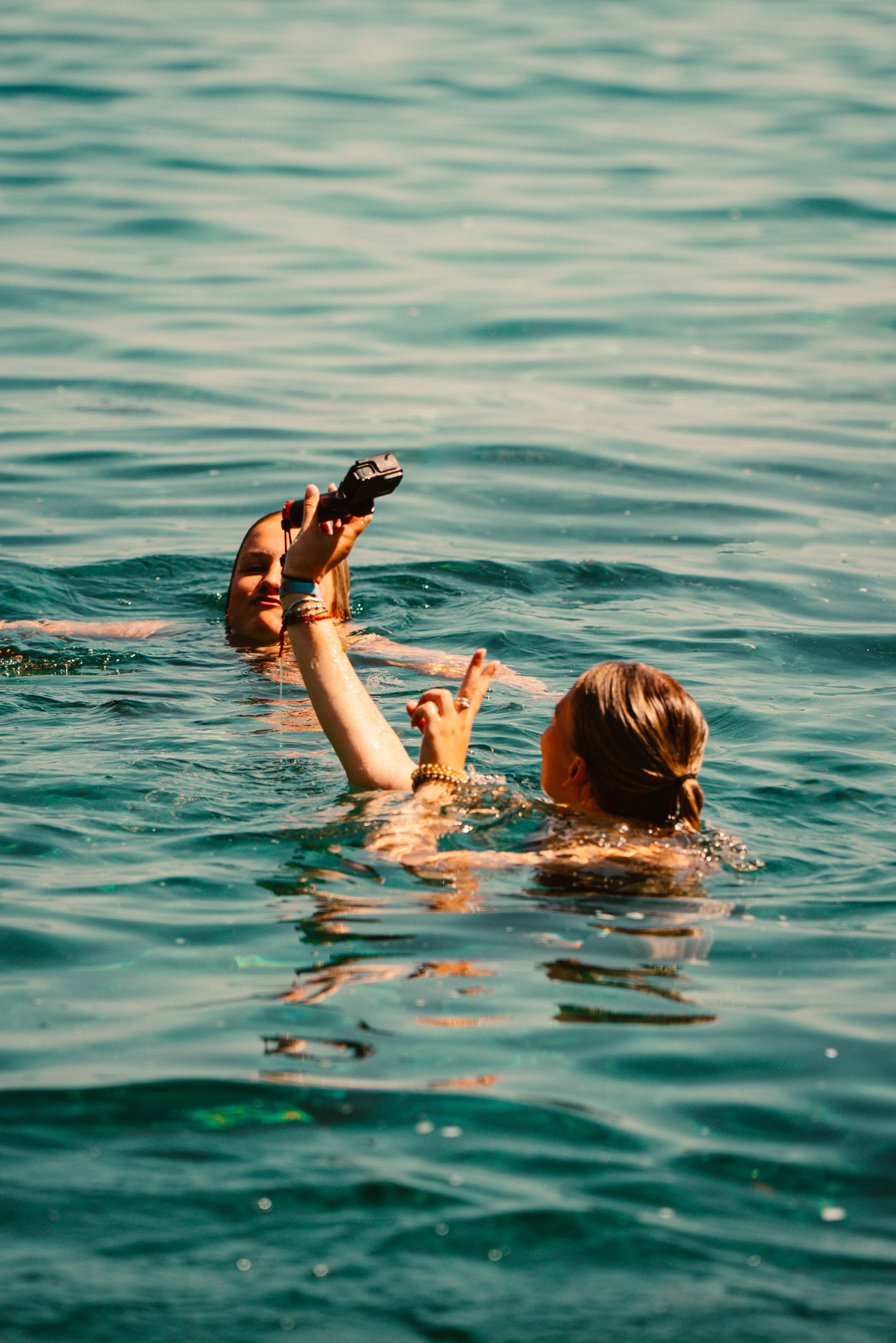 Two people swimming in clear water, one holding a camera.