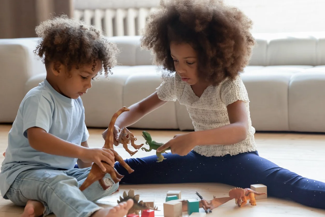 Two siblings playing with dinosaur toys