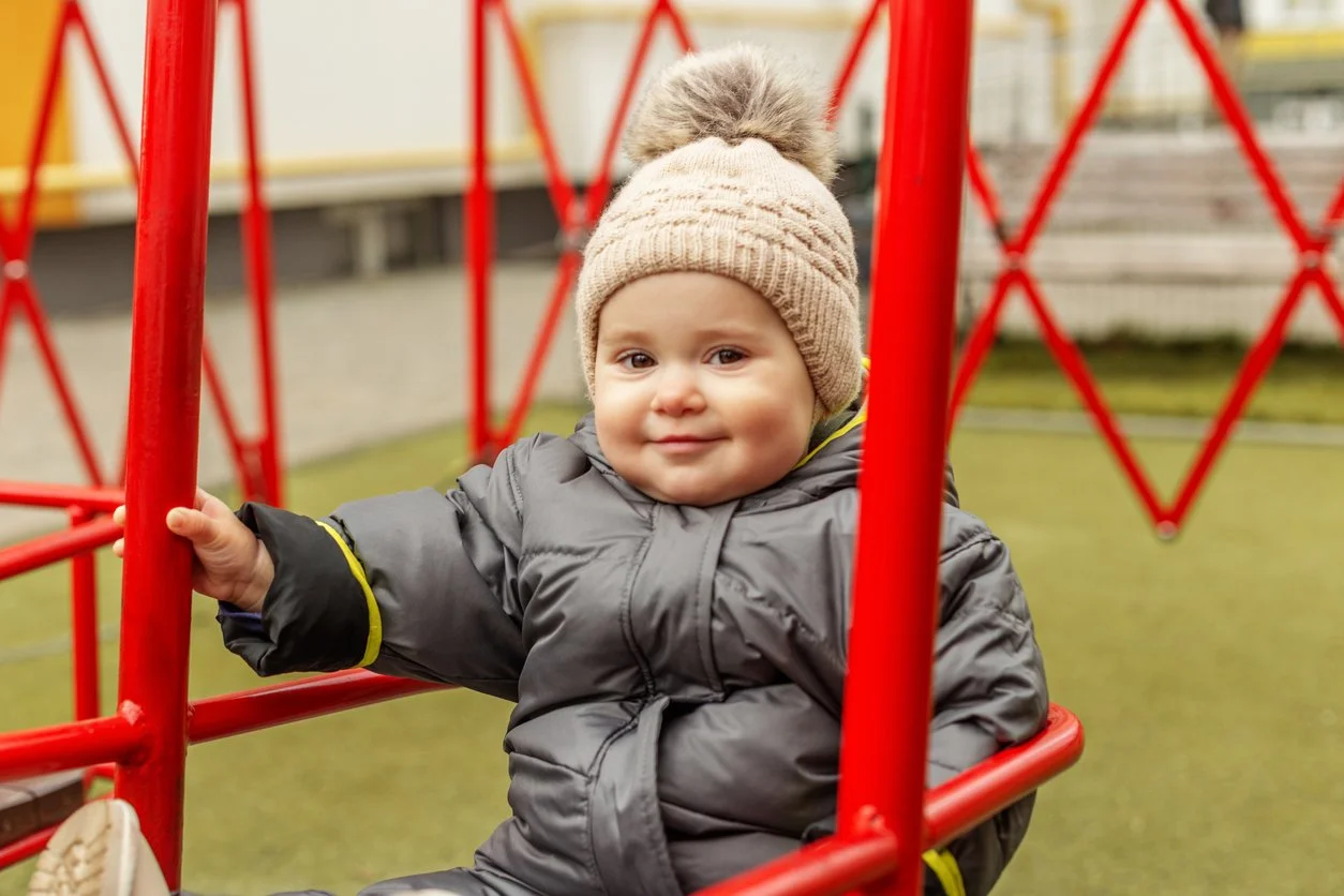 Happy baby sat in a playground with a winter hat and coat
