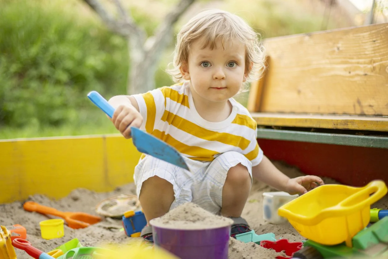 toddler boy digging in a sandpit outdoors