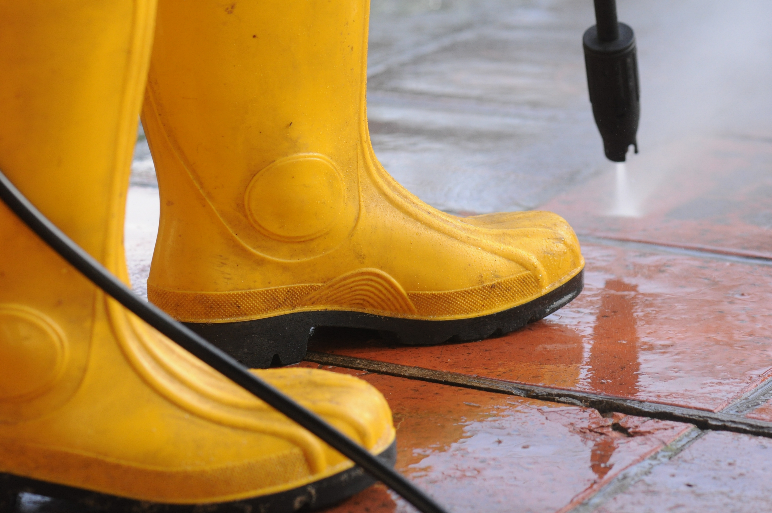 person-wearing-yellow-rubber-boots-with-high-pressure-water-nozzle-cleaning-dirt-tiles.webp