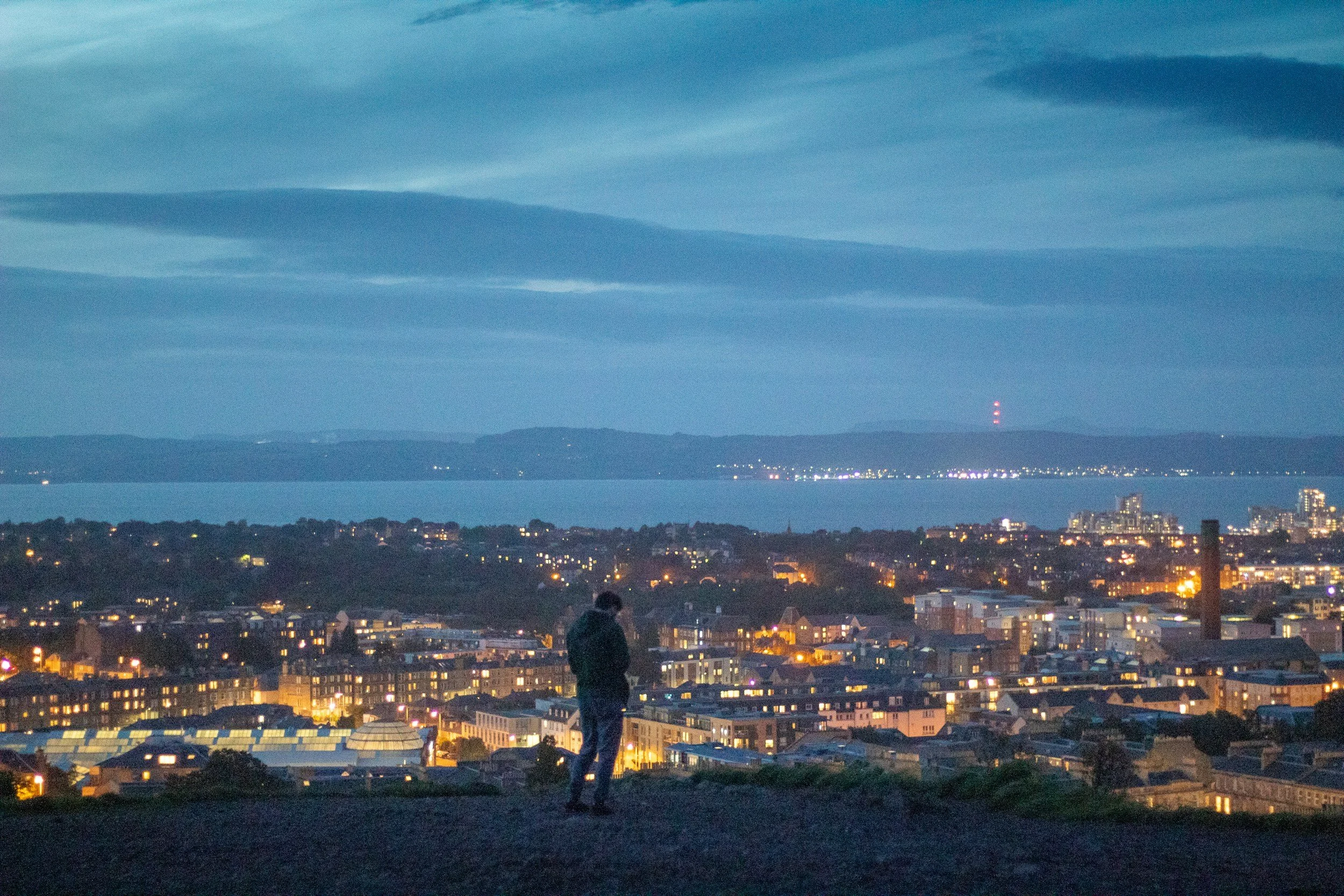 Person overlooking Edinburgh beneath a cloudy evening sky