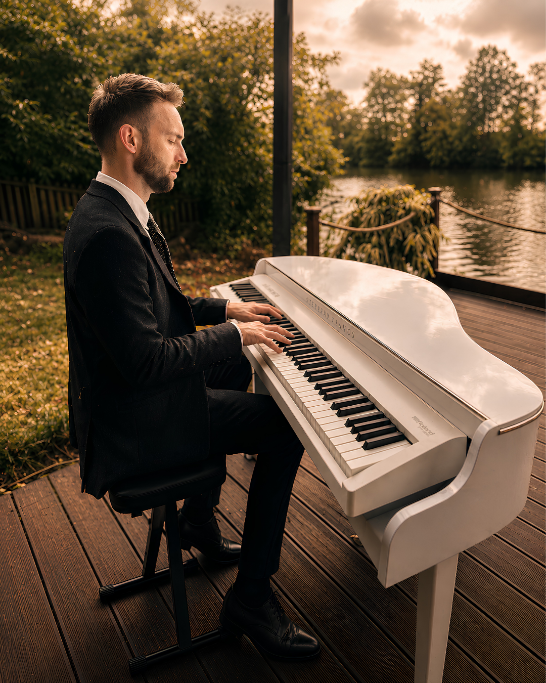 Lewis Bolland playing a white baby grand piano shell beside a lake at an outdoor wedding or private event in the South of England