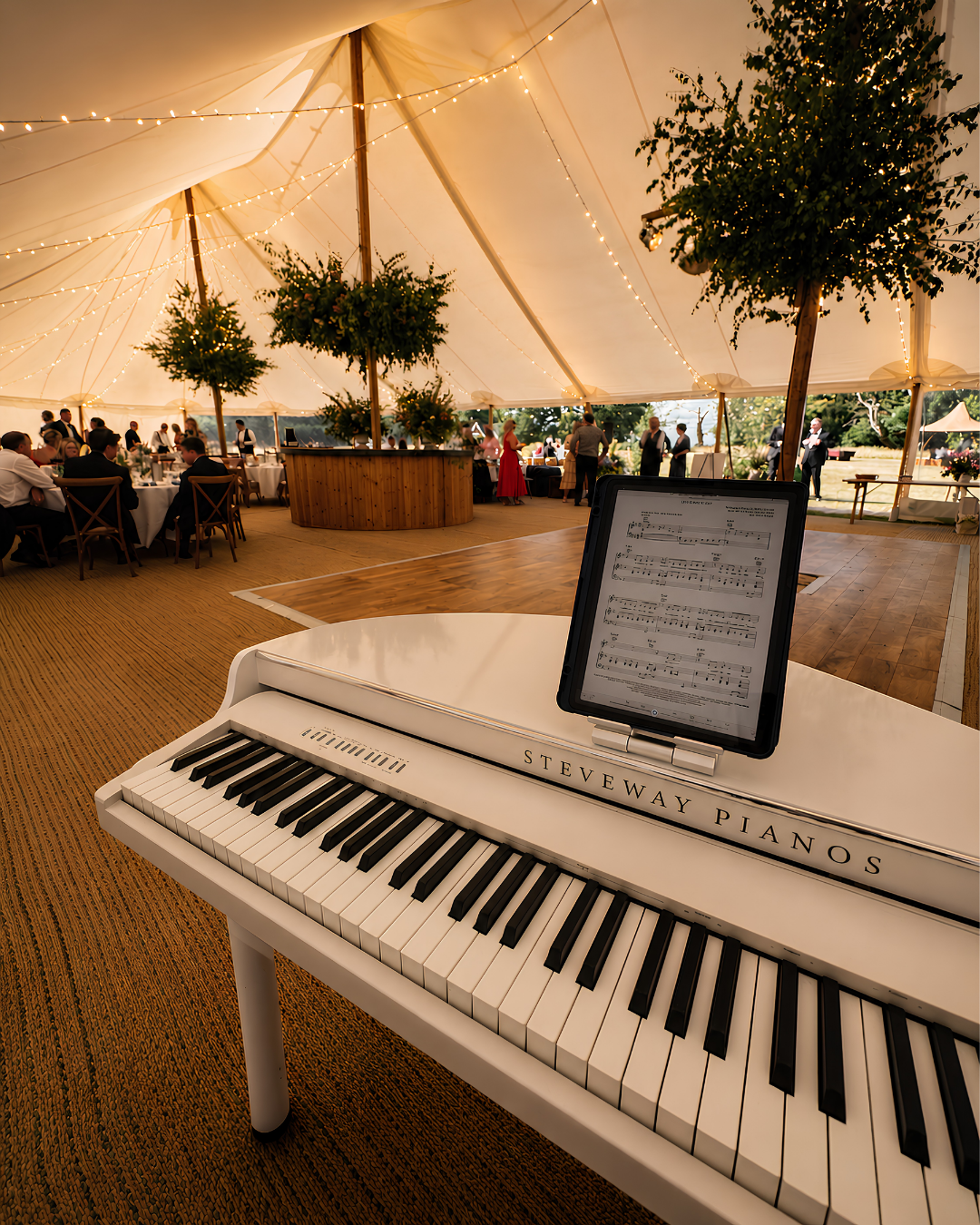 White baby grand piano shell with sheet music at a marquee wedding reception, providing elegant background piano music for guests during weddings and events