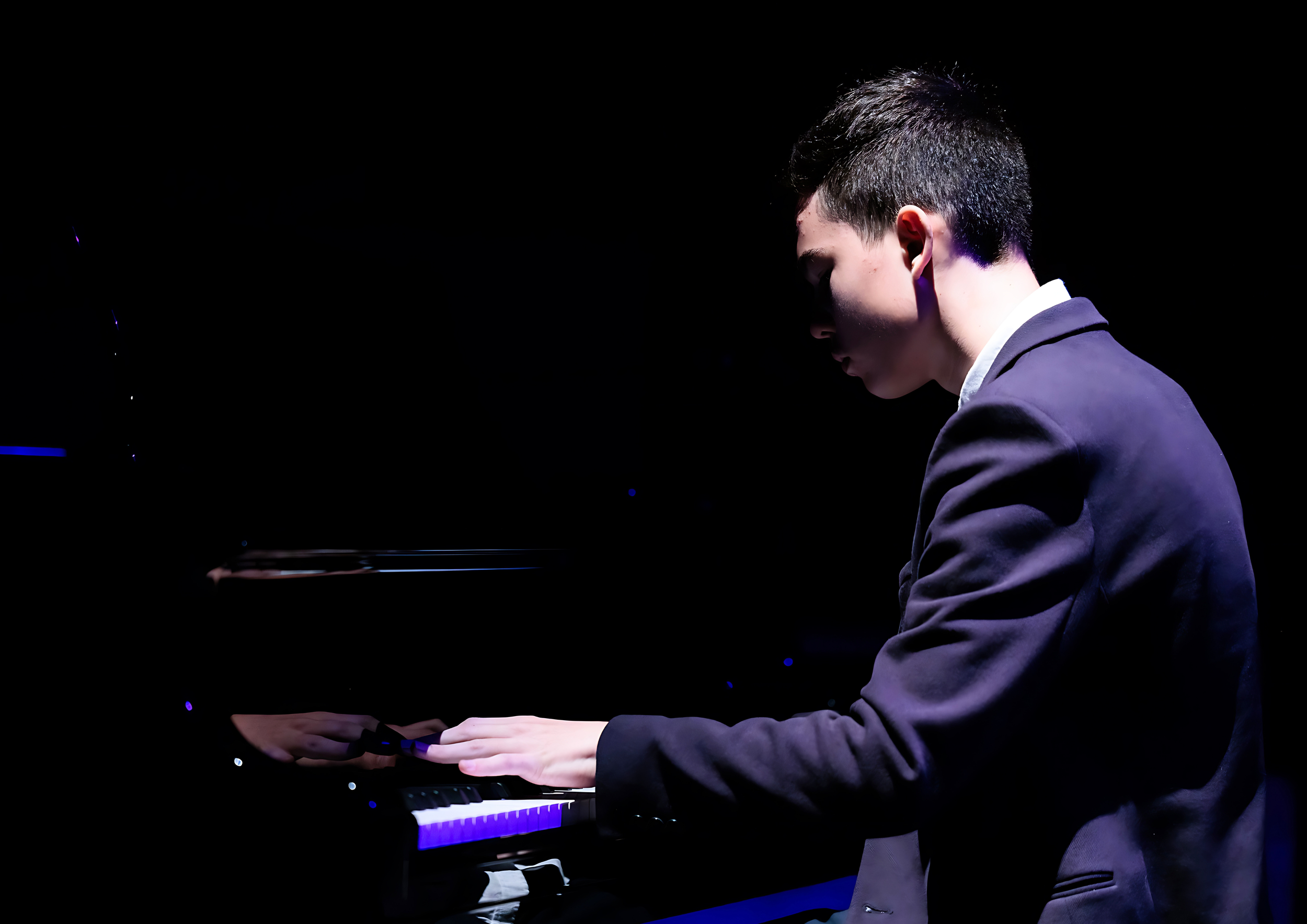 Young male student playing a Steinway Concert Grand piano at The Anvil Theatre, highlighting the 100% exam pass rate and performance success of piano lessons in Basingstoke and Tadley.