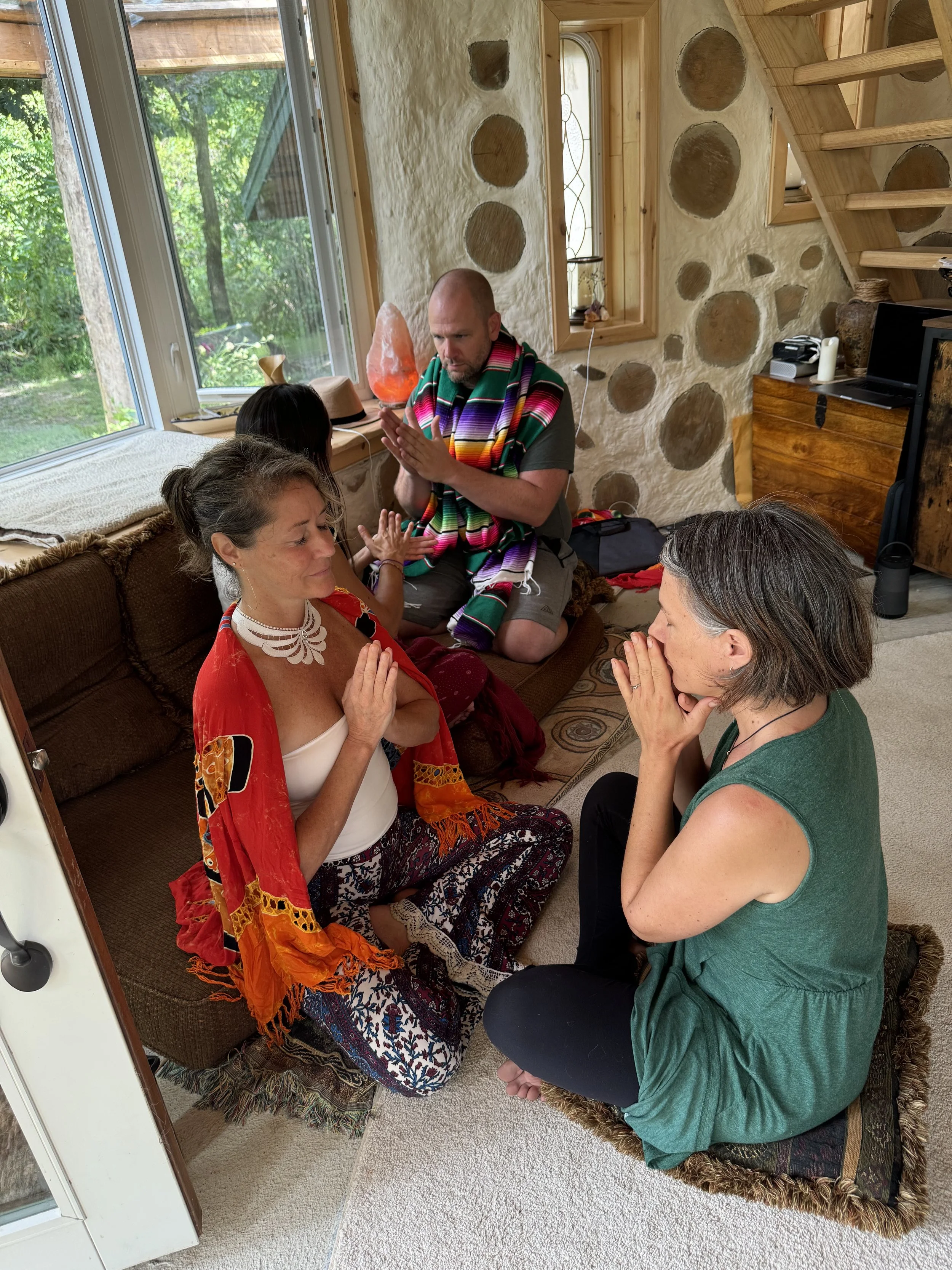 People practicing meditation or prayer in a cozy, rustic room with large windows, stone walls, and wooden accents.