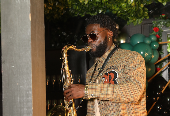 Man playing saxophone at an event with balloons and greenery in the background.