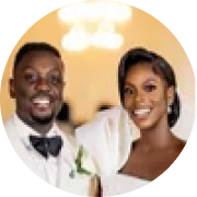 A smiling man and woman in wedding attire, standing together indoors with warm lighting.
