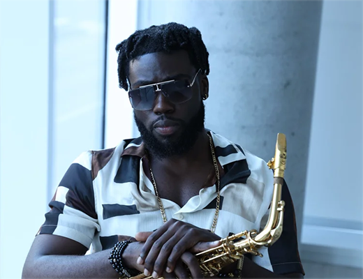 Man with sunglasses holding a gold saxophone inside a building.