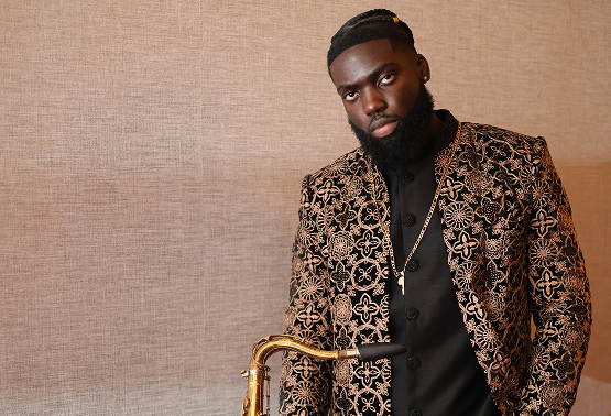 Man in ornate black and gold patterned jacket holding a saxophone.