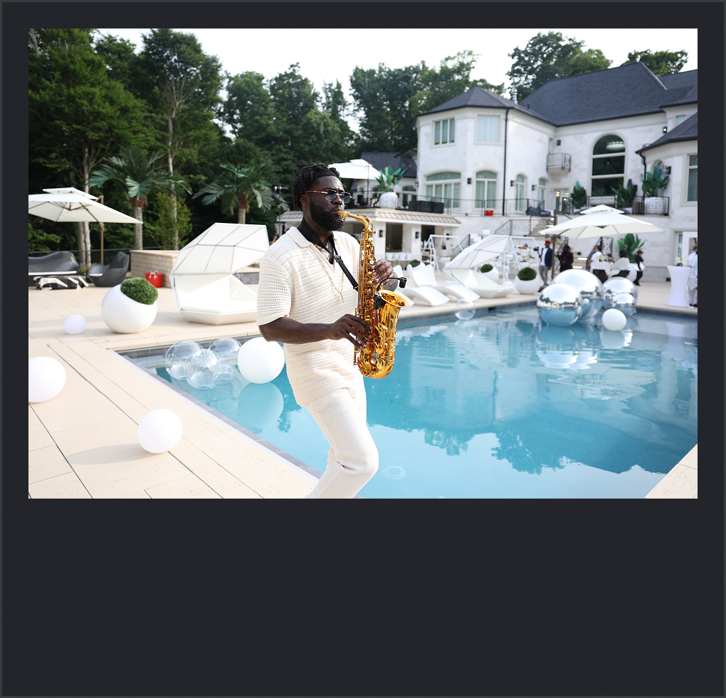 A man playing a saxophone by a luxurious swimming pool at a modern backyard estate with white furniture, umbrellas, and lush greenery.