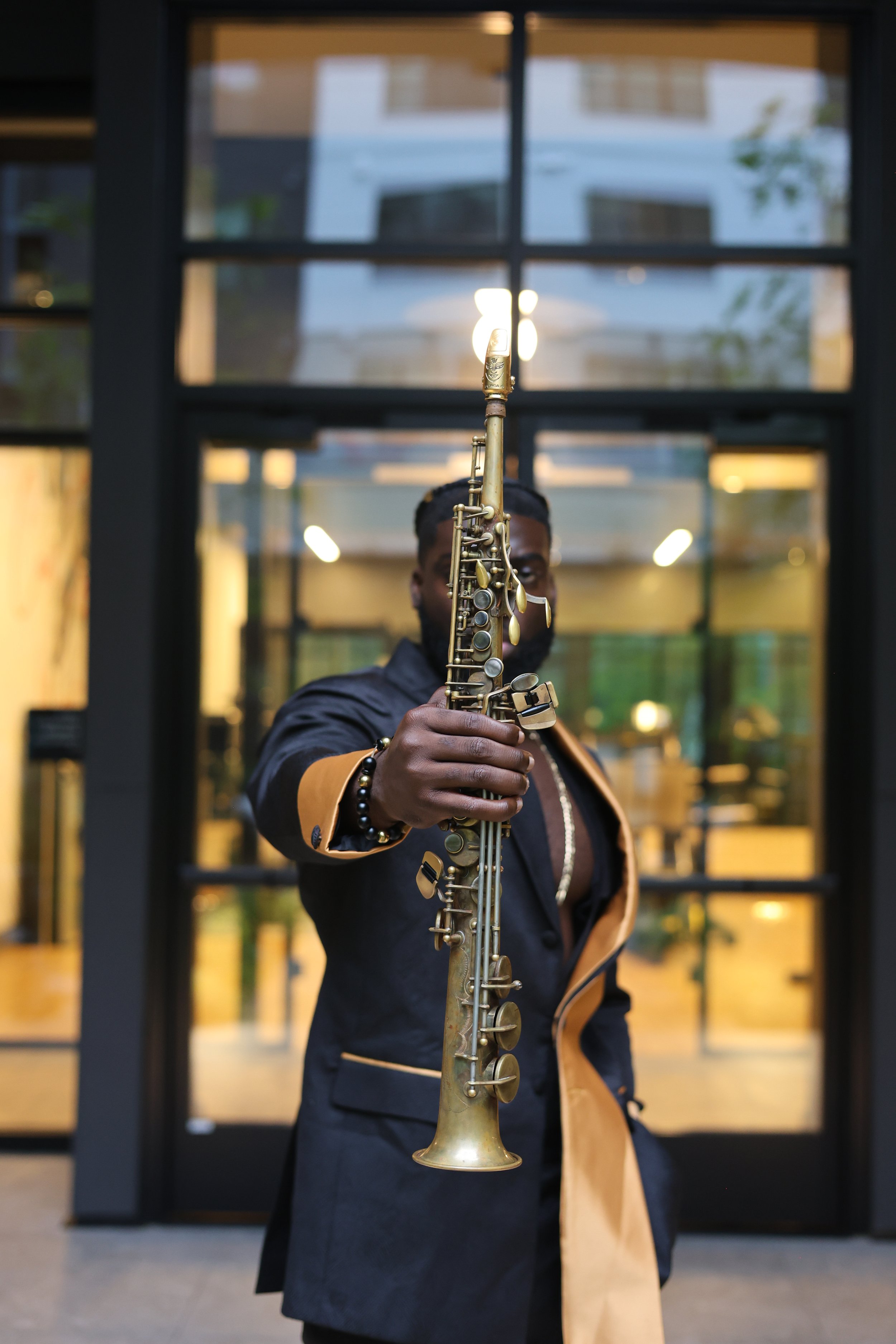 Person holding a golden saxophone in an indoor setting with large glass windows and modern architecture.