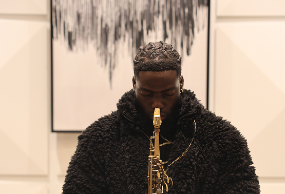A person with short curly hair playing a saxophone in an indoor setting with modern decor.