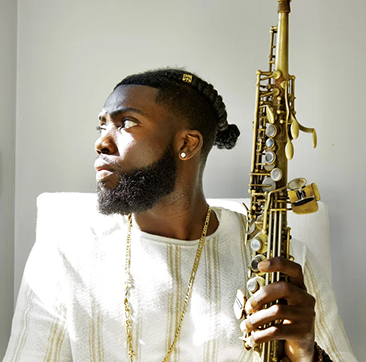 Man with a beard and gold chain holding a saxophone, looking to the side, wearing a white shirt, against a plain background.
