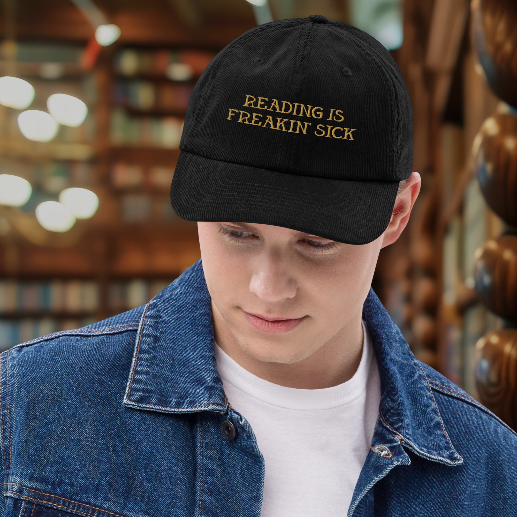 Close-up of person wearing black baseball cap with embroidered text 'READING IS FREAKIN' SICK' in gold, indoors with blurred bookshelves and lights in background.