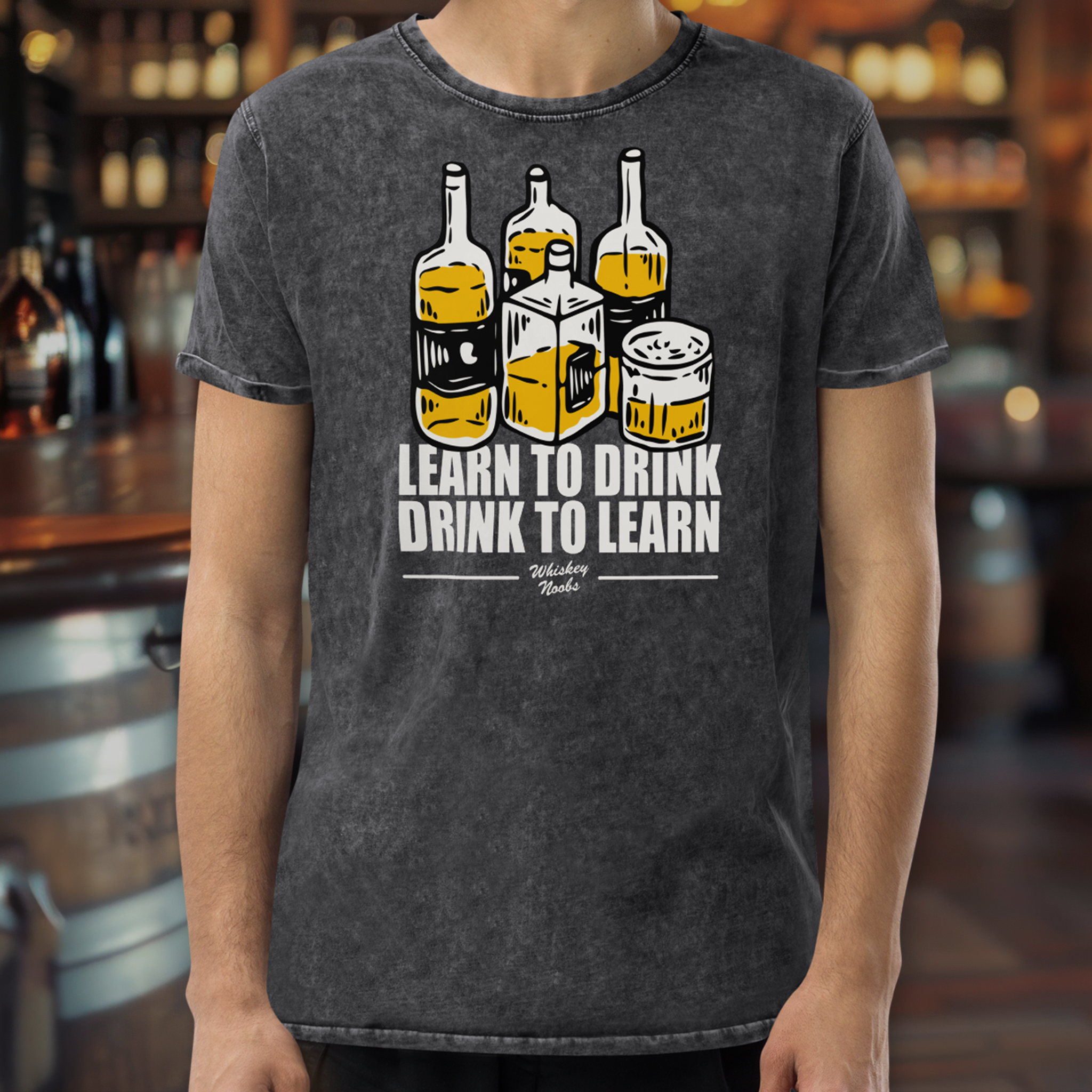 A person wearing a gray t-shirt with a graphic of whiskey bottles and a glass. The text on the shirt says 'Learn to Drink, Drink to Learn' and 'Whiskey Nook'.