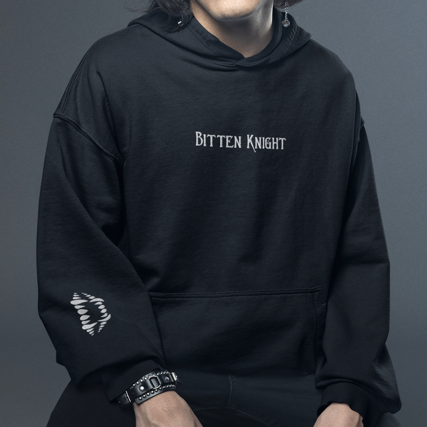 A person wearing a black hoodie with the words "Bitten Knight" embroidered on the chest, standing against a dark gray background.