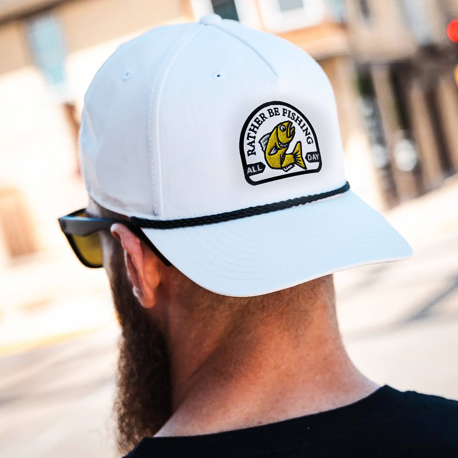 Person wearing a white cap with a fishing-themed logo and text, with sunglasses hanging from the collar.