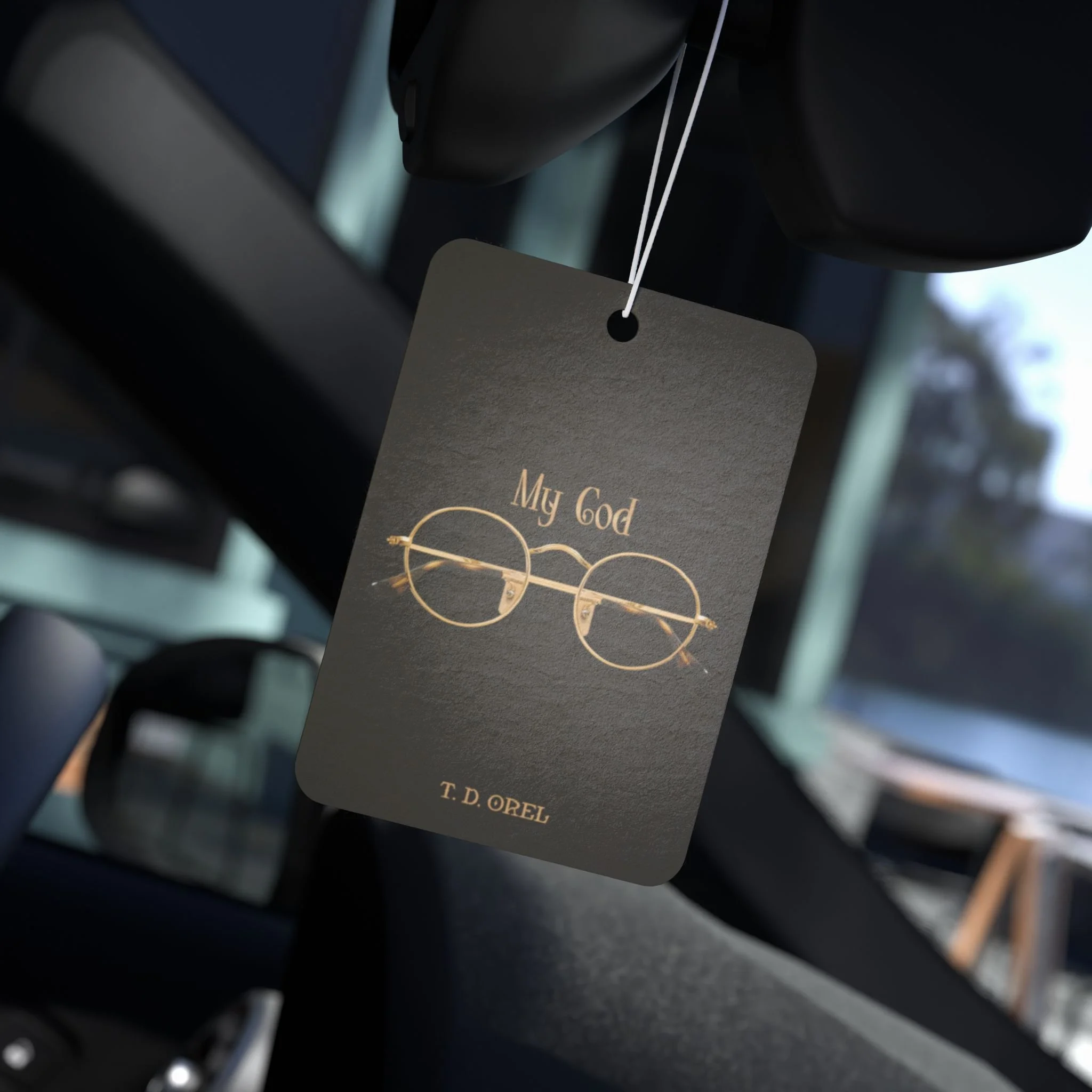 Close-up of a black card with the text 'My God' along with a gold infinity symbol and the name T. D. Orel, hanging from a string in a dark environment.