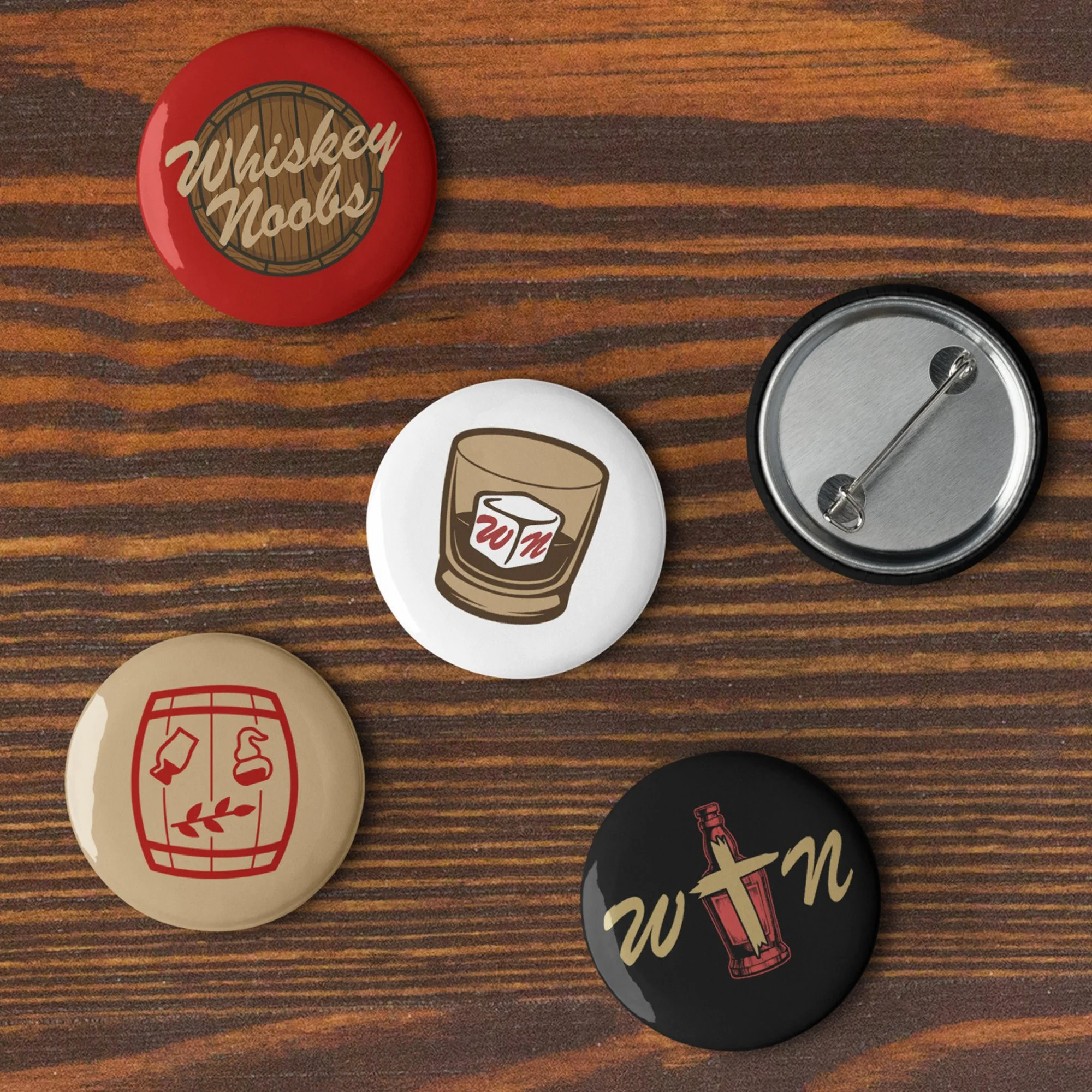 Collection of circular pins featuring whiskey and drinking-related graphics and text, placed on a wooden surface.