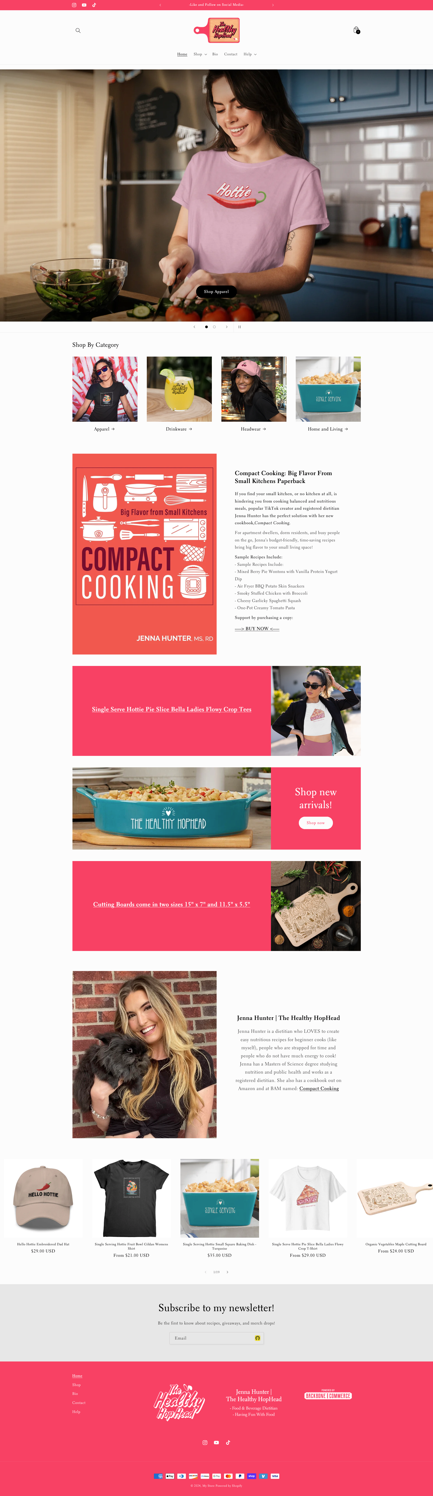 A woman smiling while preparing food in a kitchen with blue cabinets and a stainless steel refrigerator, wearing a purple t-shirt with a hot chili pepper graphic and the word 'Hottie' on it.