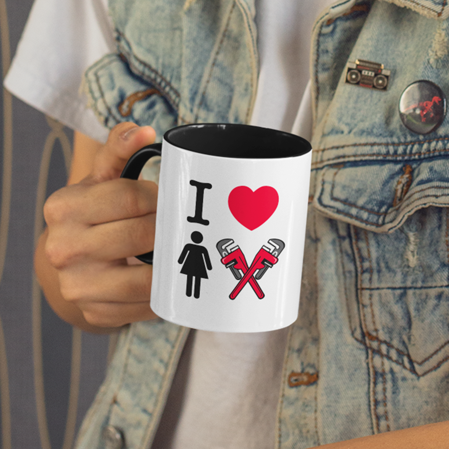 Person holding a white mug with a design that says 'I love' with a female gender symbol and two large red pipe wrenches forming a bow.