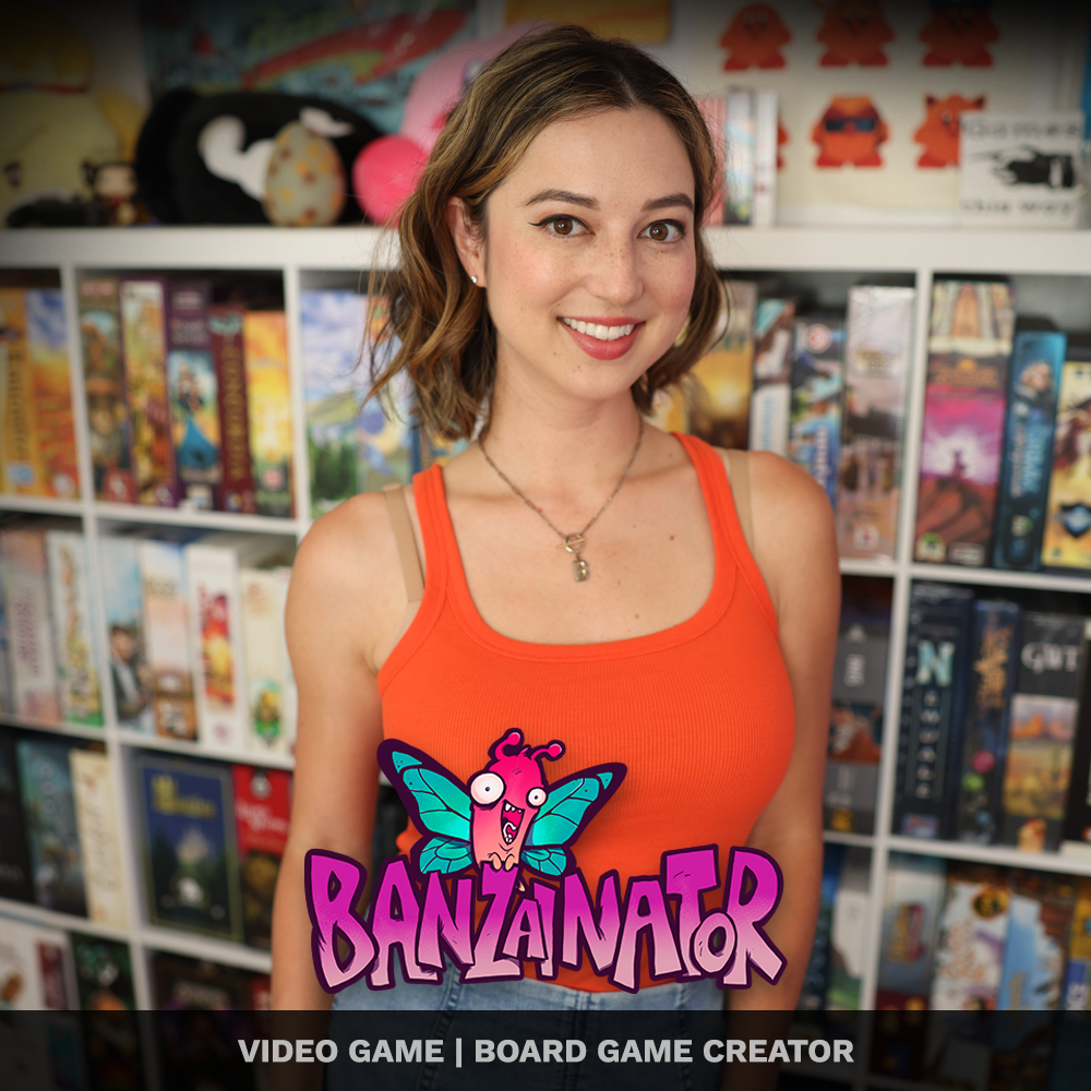 A young woman with shoulder-length brown hair wearing an orange tank top and a necklace, standing in front of a bookshelf filled with board games and toys, smiling at the camera.