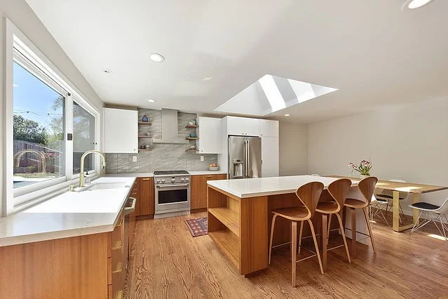 Modern kitchen with white cabinets, wooden flooring, a skylight, and a central island with stools.