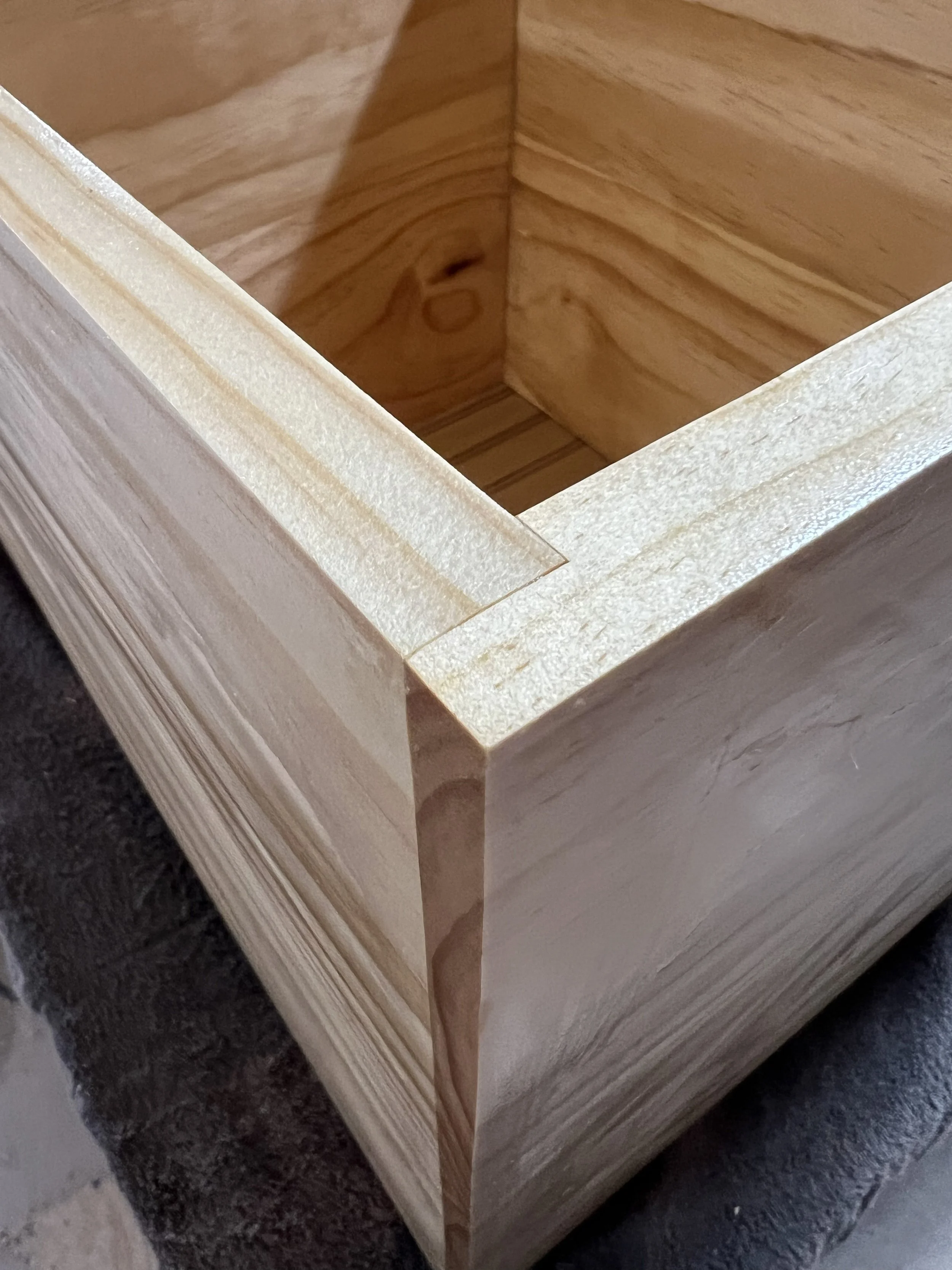 Close-up of a wooden box with smooth, finished sides and an unfinished interior, showing the corner joint, placed on a dark work surface.