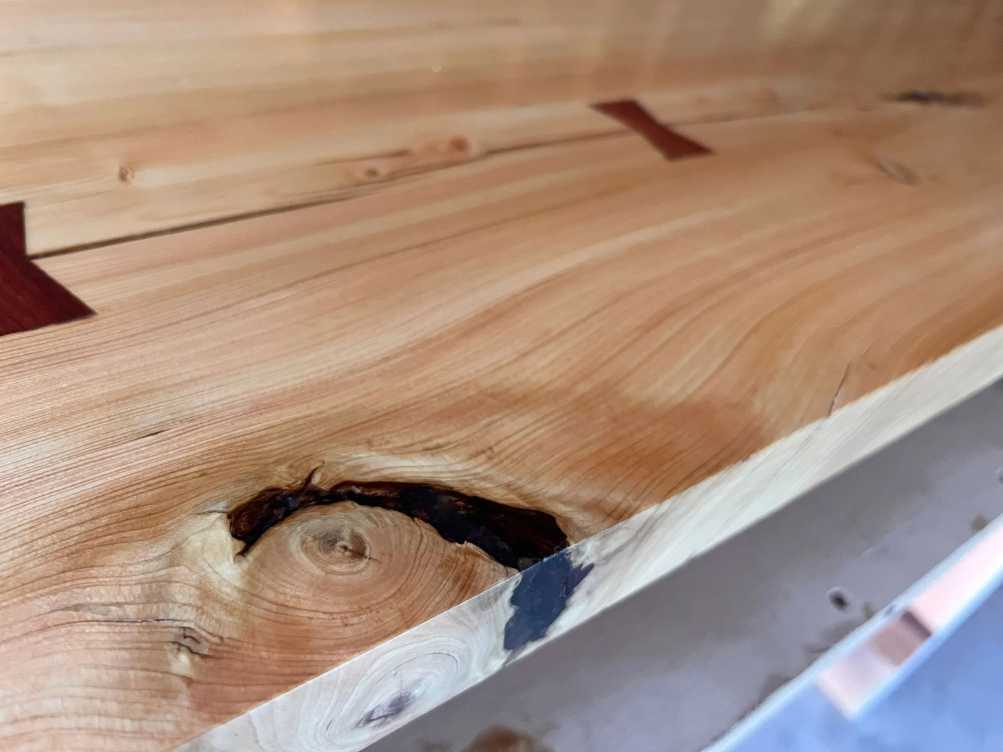 Close-up photo of unfinished wood with a knot and a crack, showing natural wood grain and some darkened areas.