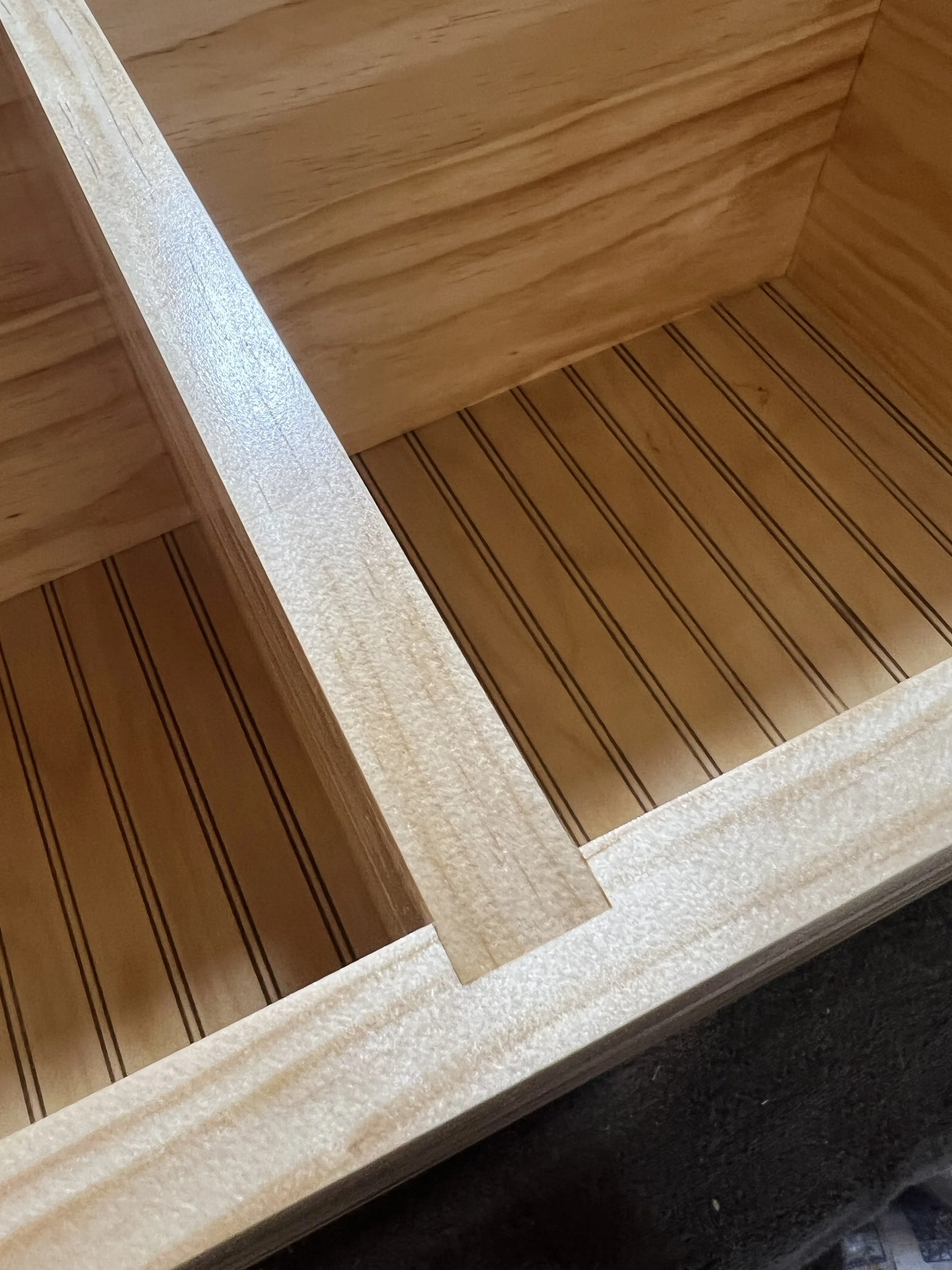 Close-up of a wooden drawer with a natural finish, showing the inside with a wood grain pattern and support divider.