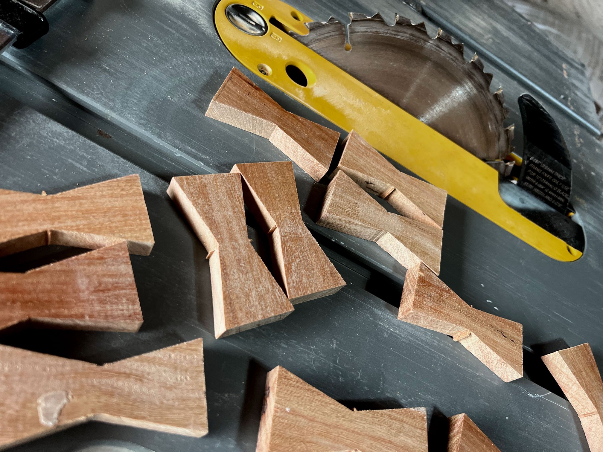 Wooden pieces on a saw table with a yellow handsaw in the background.
