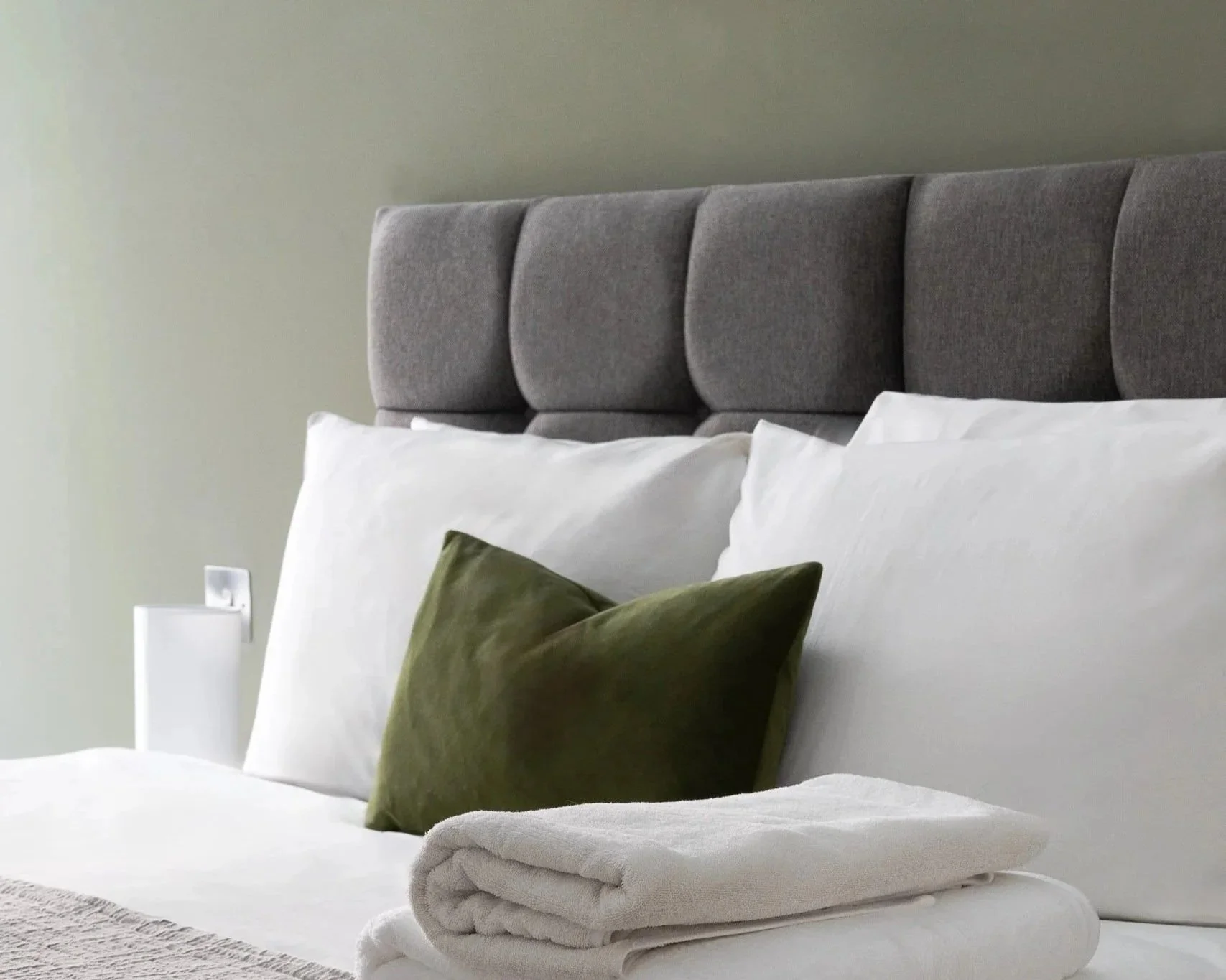 A bed with a green pillow and grey headboard