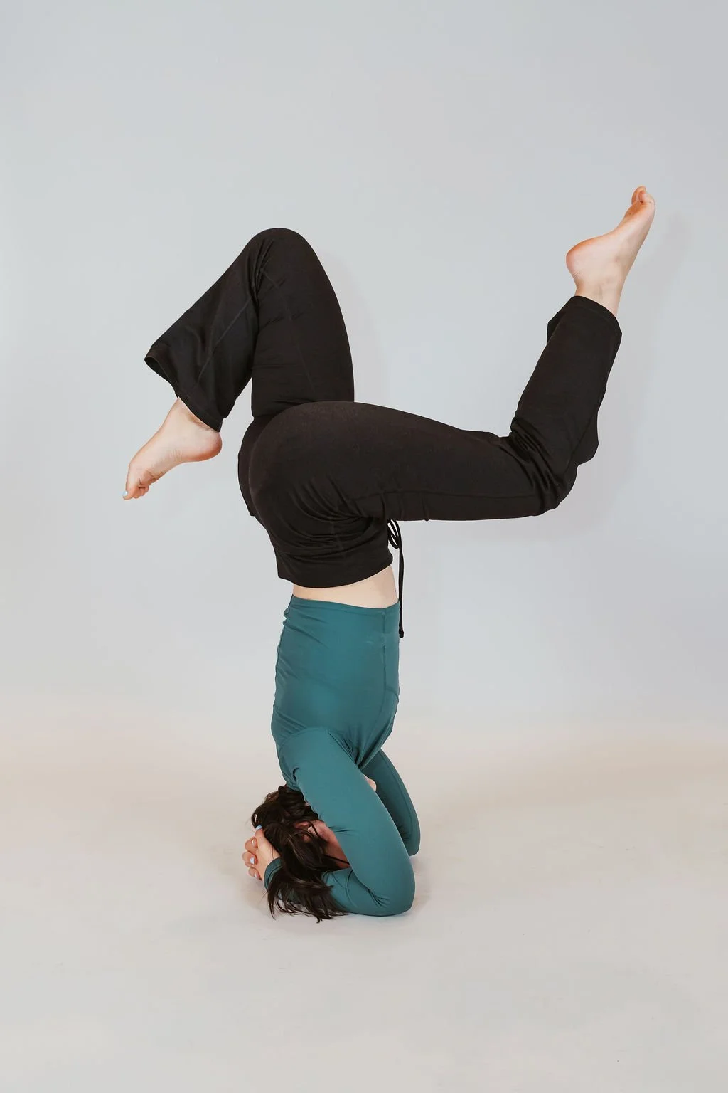 Woman practicing a headstand yoga pose against a plain light gray background.