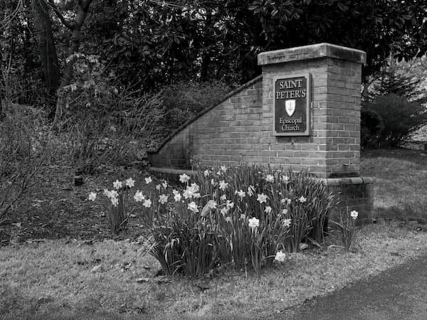Brick signpost for Saint Peter's Episcopal Church with flowers in front and trees in the background.