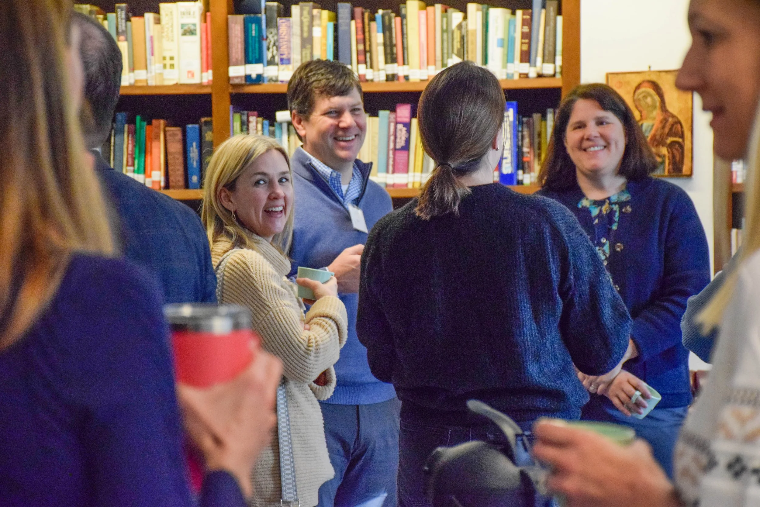 Group of people smiling and conversing in a library bookshelf background.
