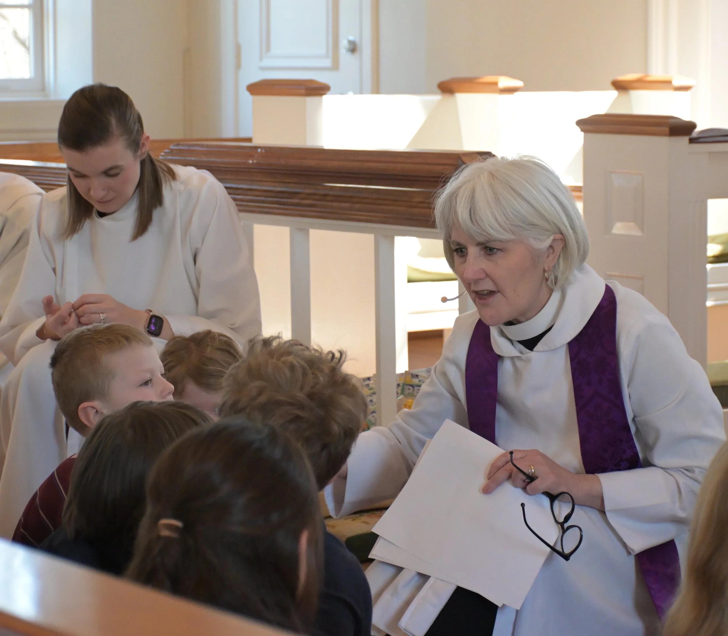 A woman dressed in religious attire engaging with children in a church or chapel setting during a religious service or class.