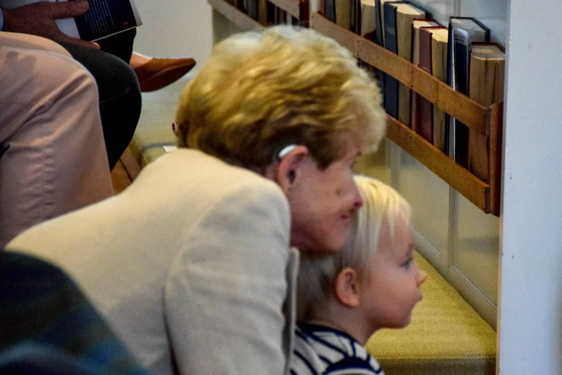 People sitting on the floor, looking at something out of the frame, with a bookshelf in the background.