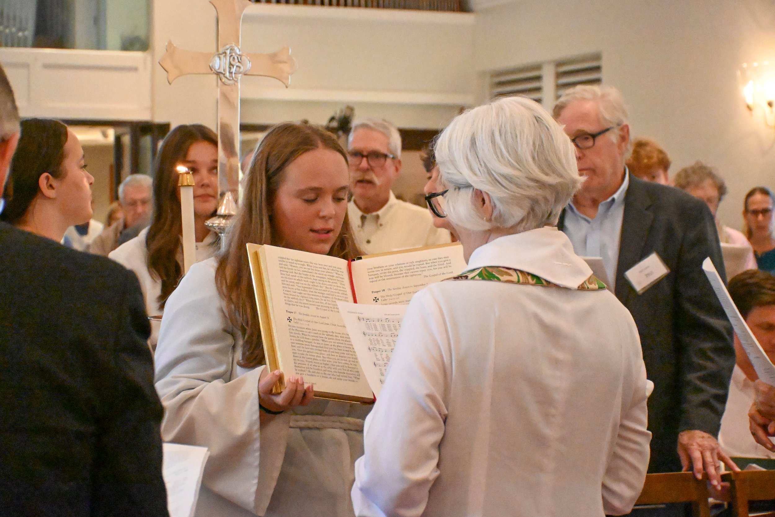 People gathered around a woman reading from a large religious book at a church service.