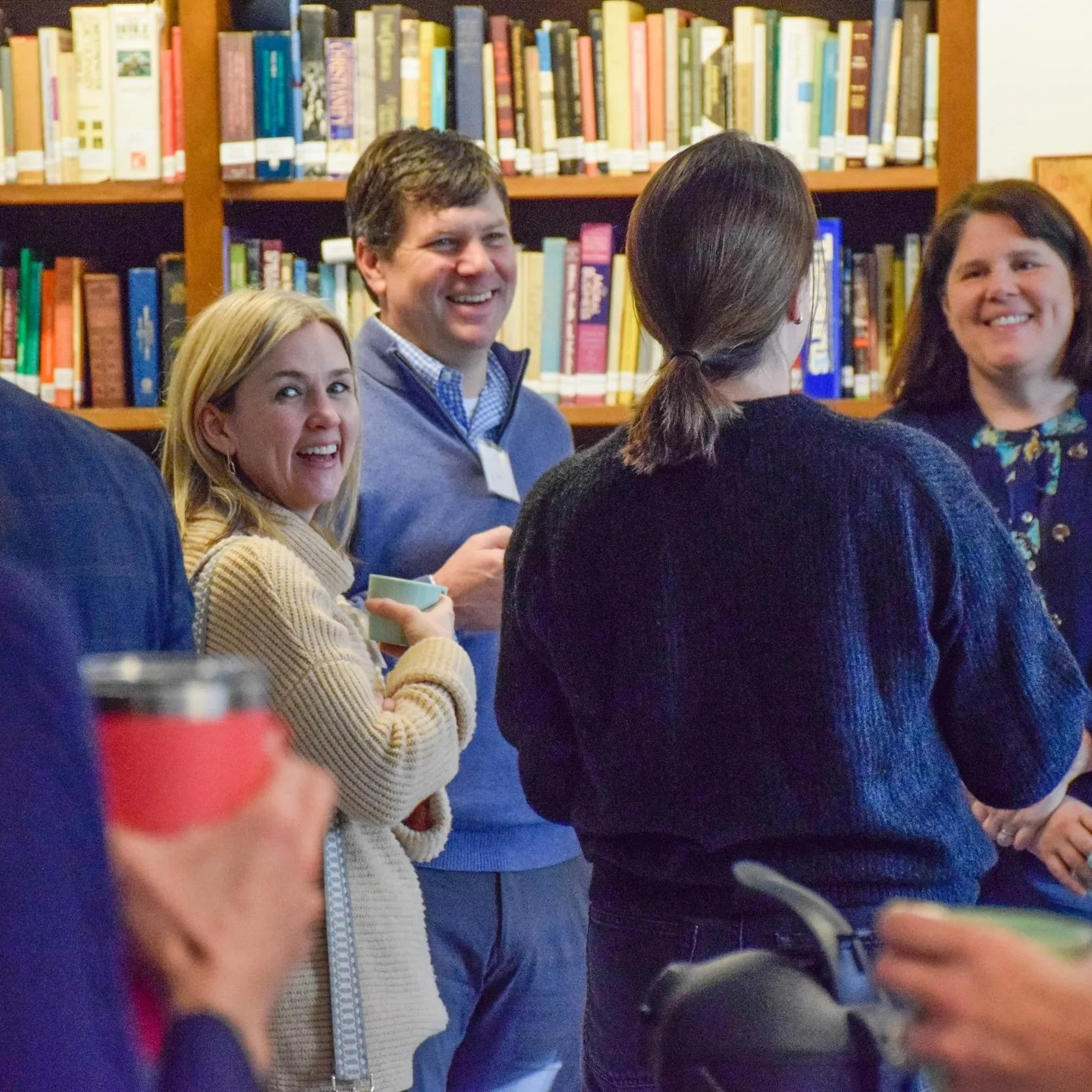 Group of four people standing in front of bookshelves, smiling and engaging in conversation, in a library setting.