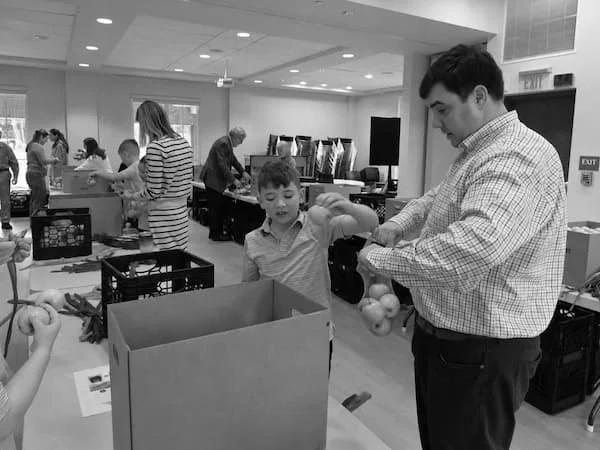 People volunteering at a donation or charity event, packing items into boxes in a large indoor space.