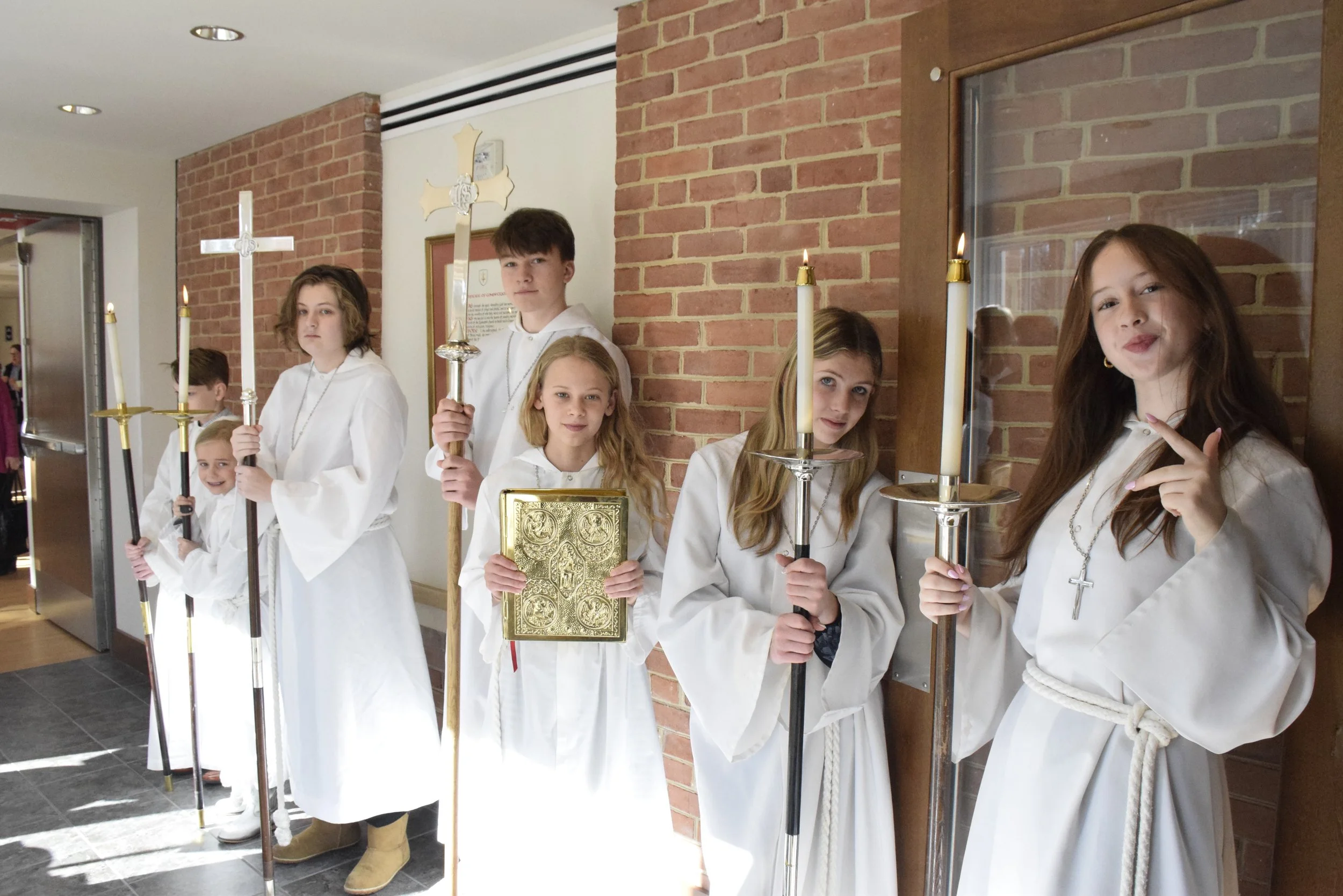 Children dressed in white robes holding candles and religious items during a ceremony inside a church.