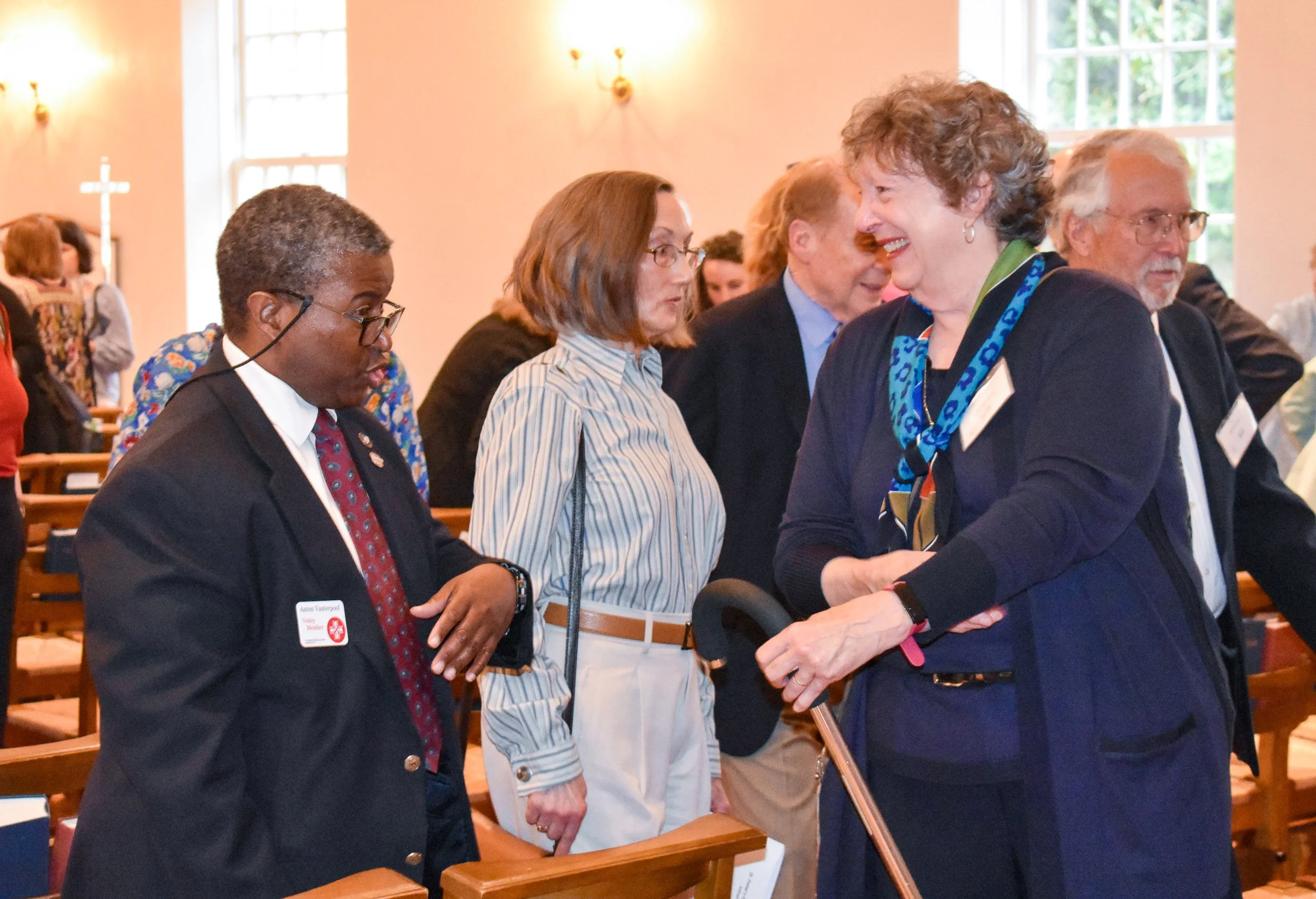 People standing and talking in a church or conference room, engaging in conversation and smiling.