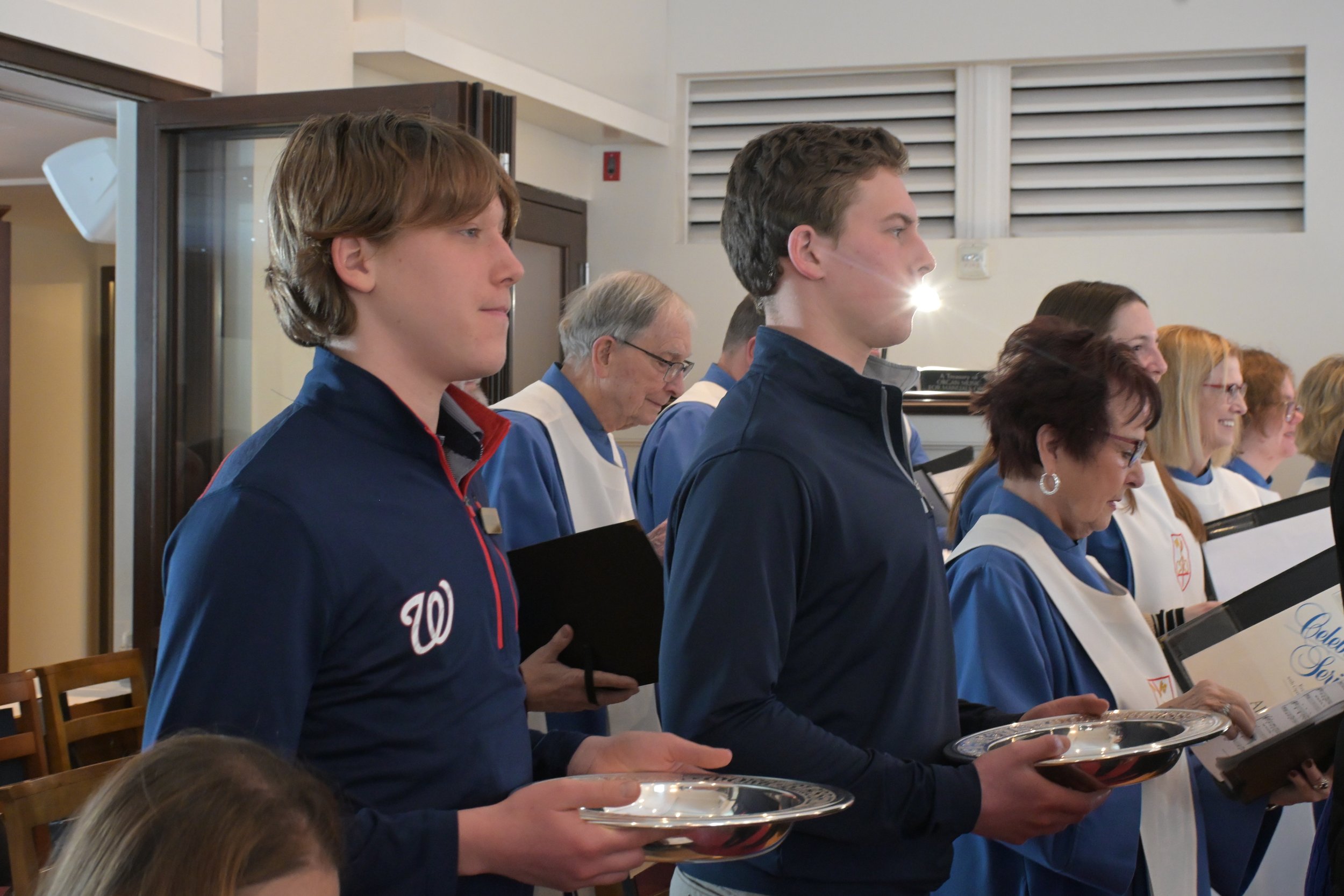 People standing in a row holding silver trays during a formal ceremony, with some wearing blue and white uniforms and others holding certificates.