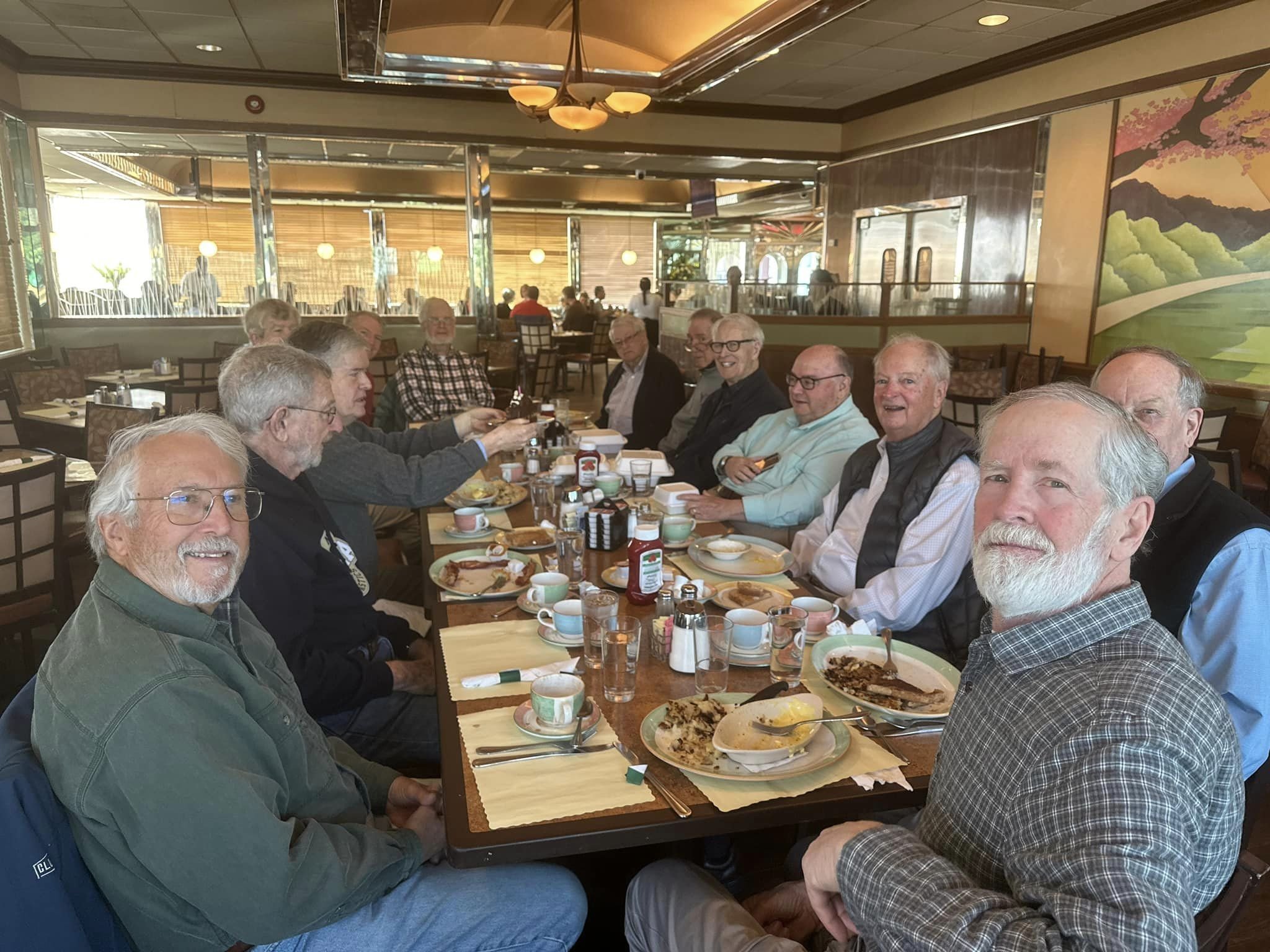 A group of elderly men sitting around a dining table in a restaurant, with plates of food and drinks on the table.