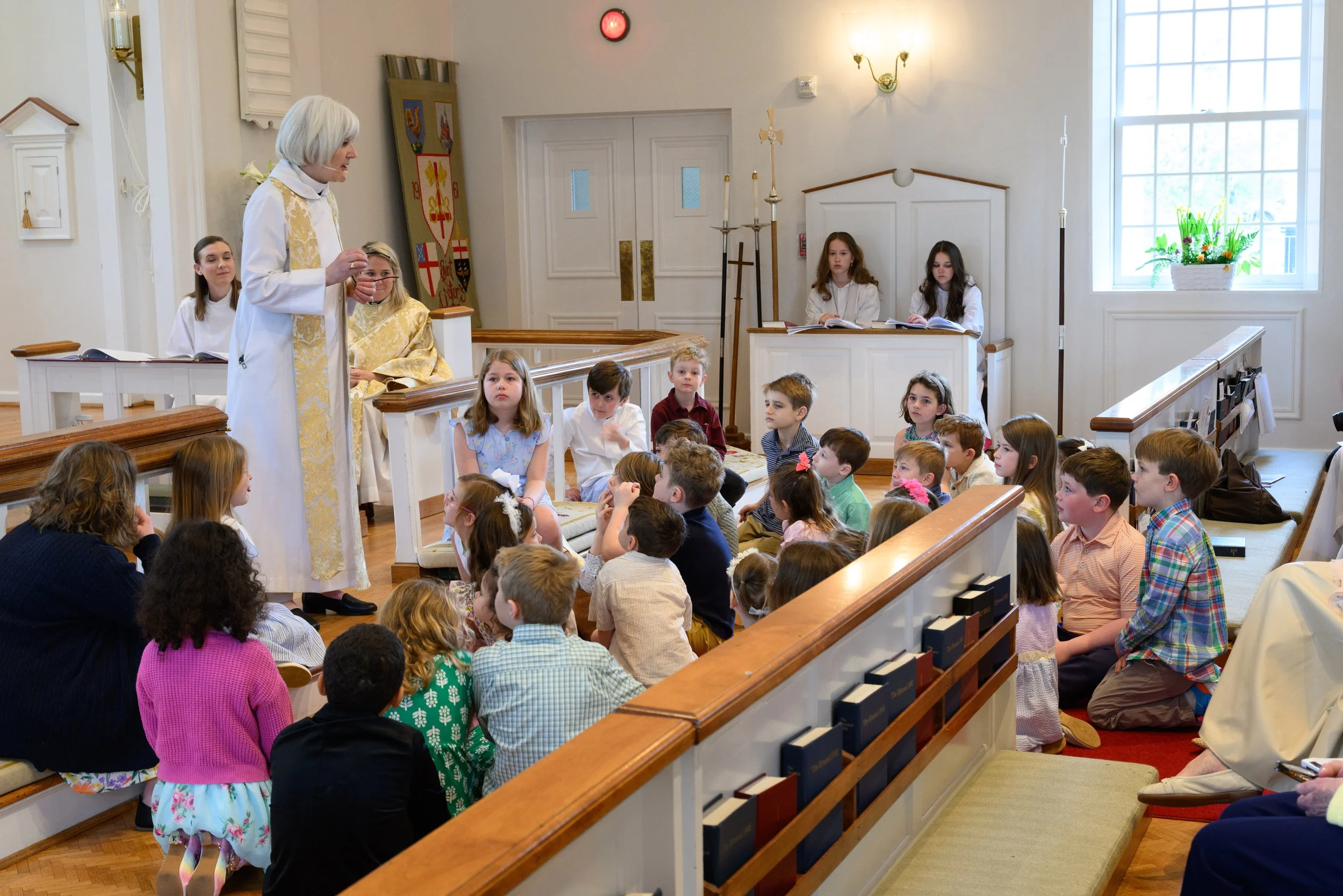 A priest speaking to a group of children during a church service in a chapel.