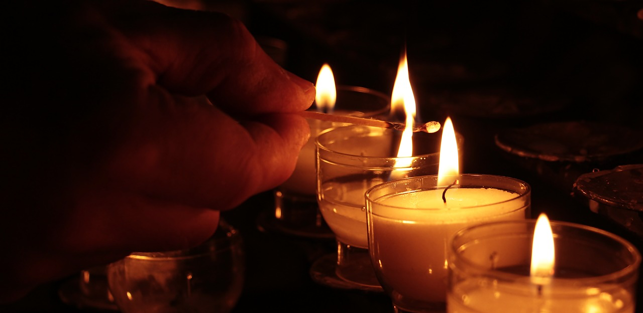 A hand lighting candles in glass holders with a matchstick.